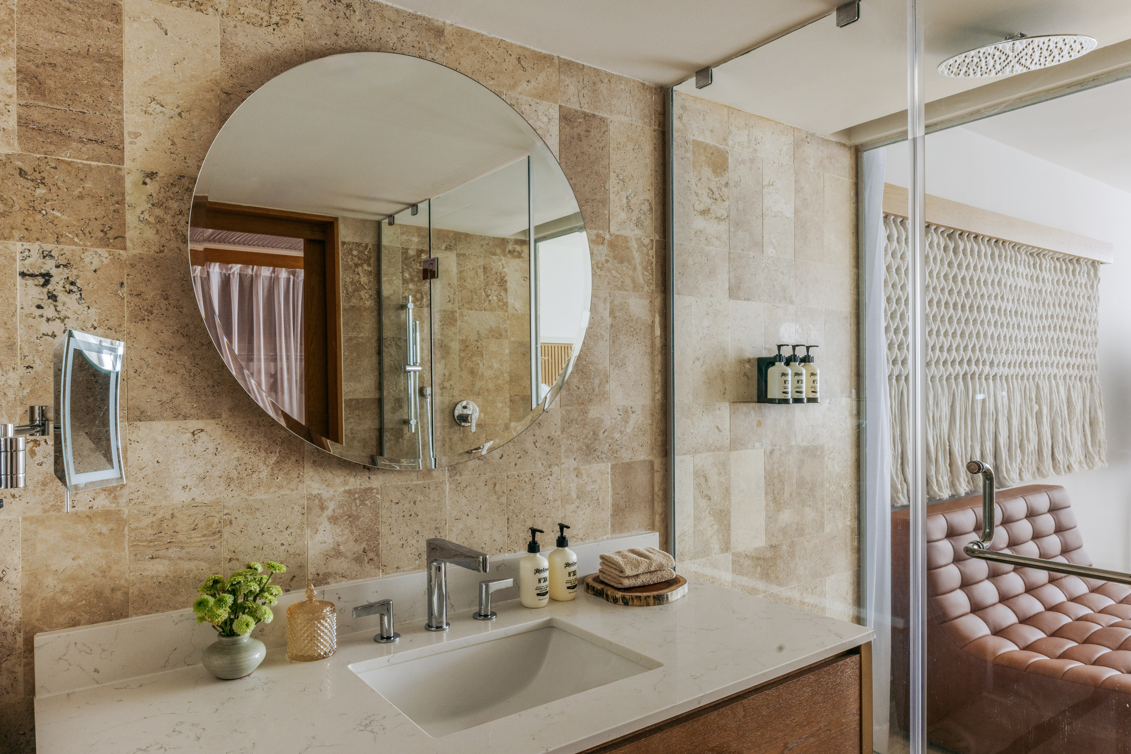 Contemporary bathroom vanity with circular mirror, stone tiles, and glass shower.