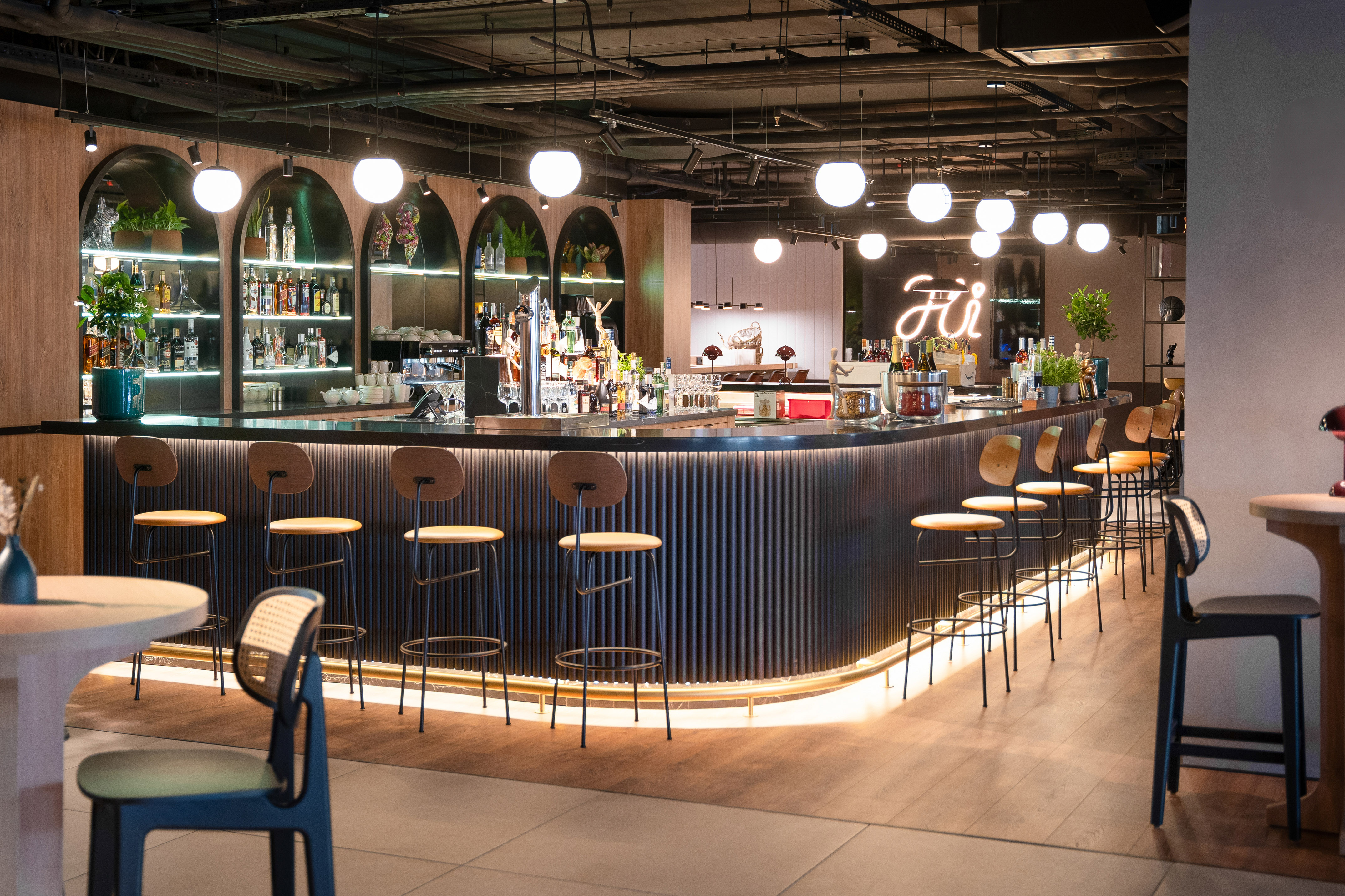 Modern hotel bar with stylish lighting, curved counter, and 'Hi' neon sign.