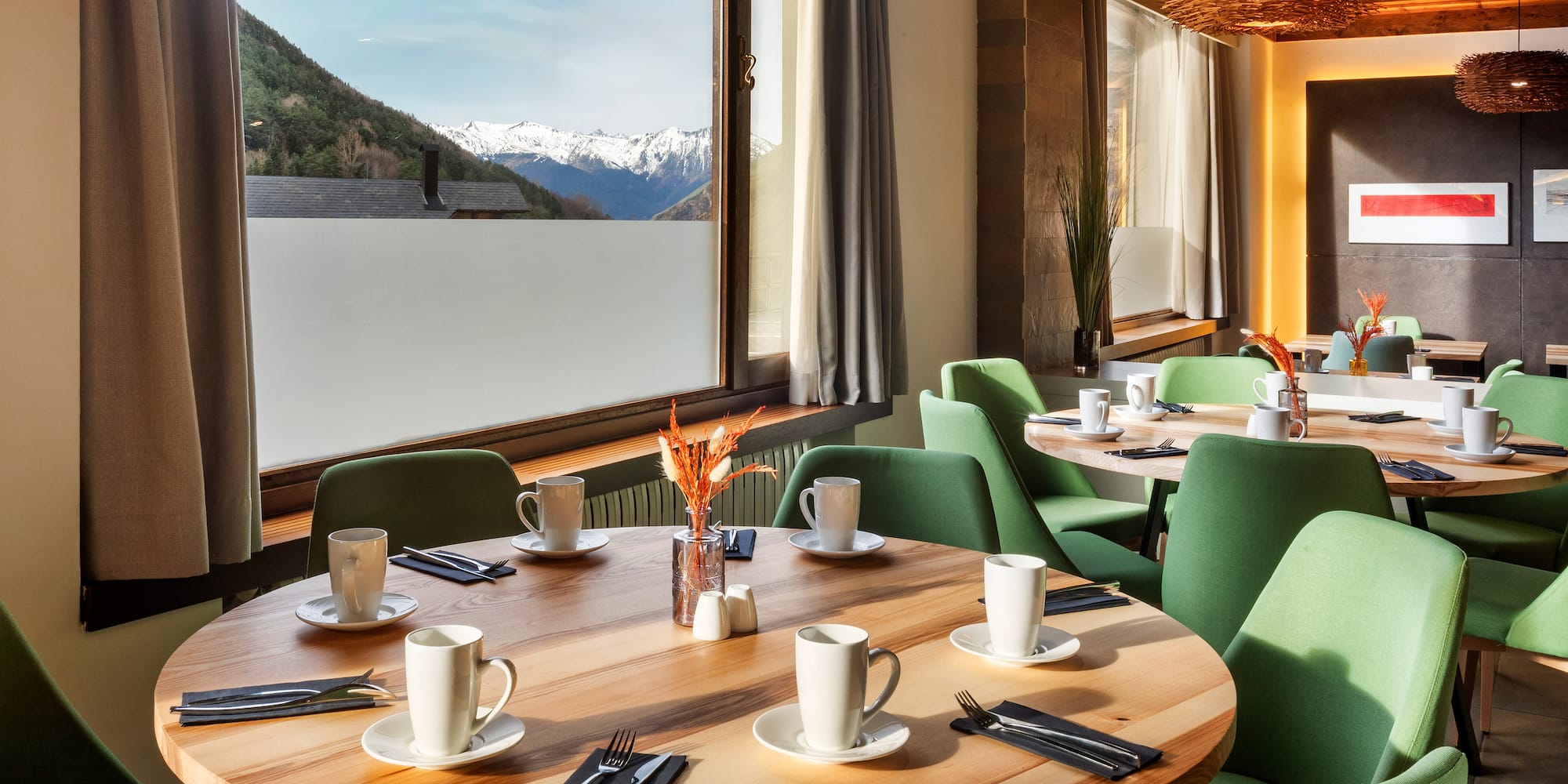 a table with white cups and green chairs in a room with a view of mountains