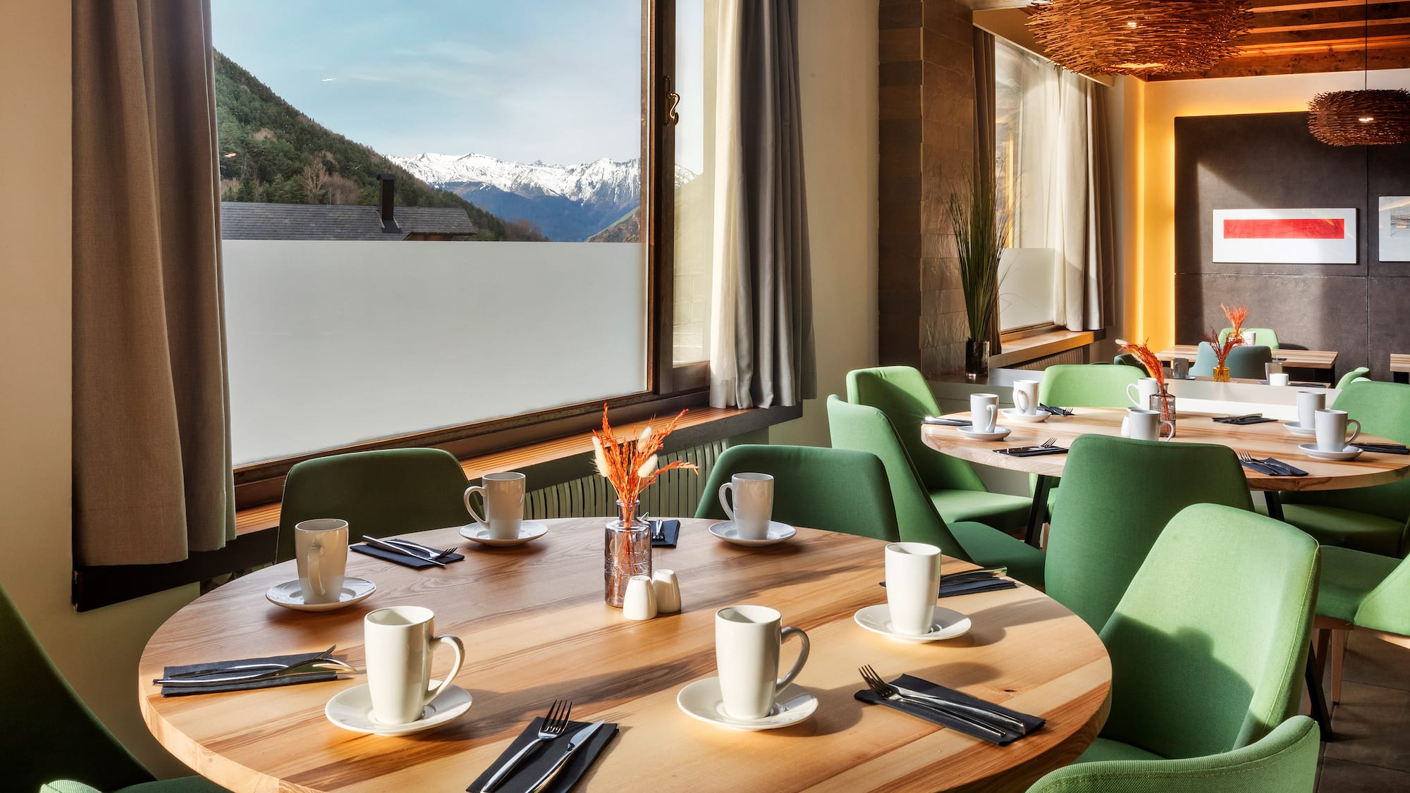 a table with white cups and green chairs in a room with a view of mountains