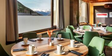 a table with white cups and green chairs in a room with a view of mountains