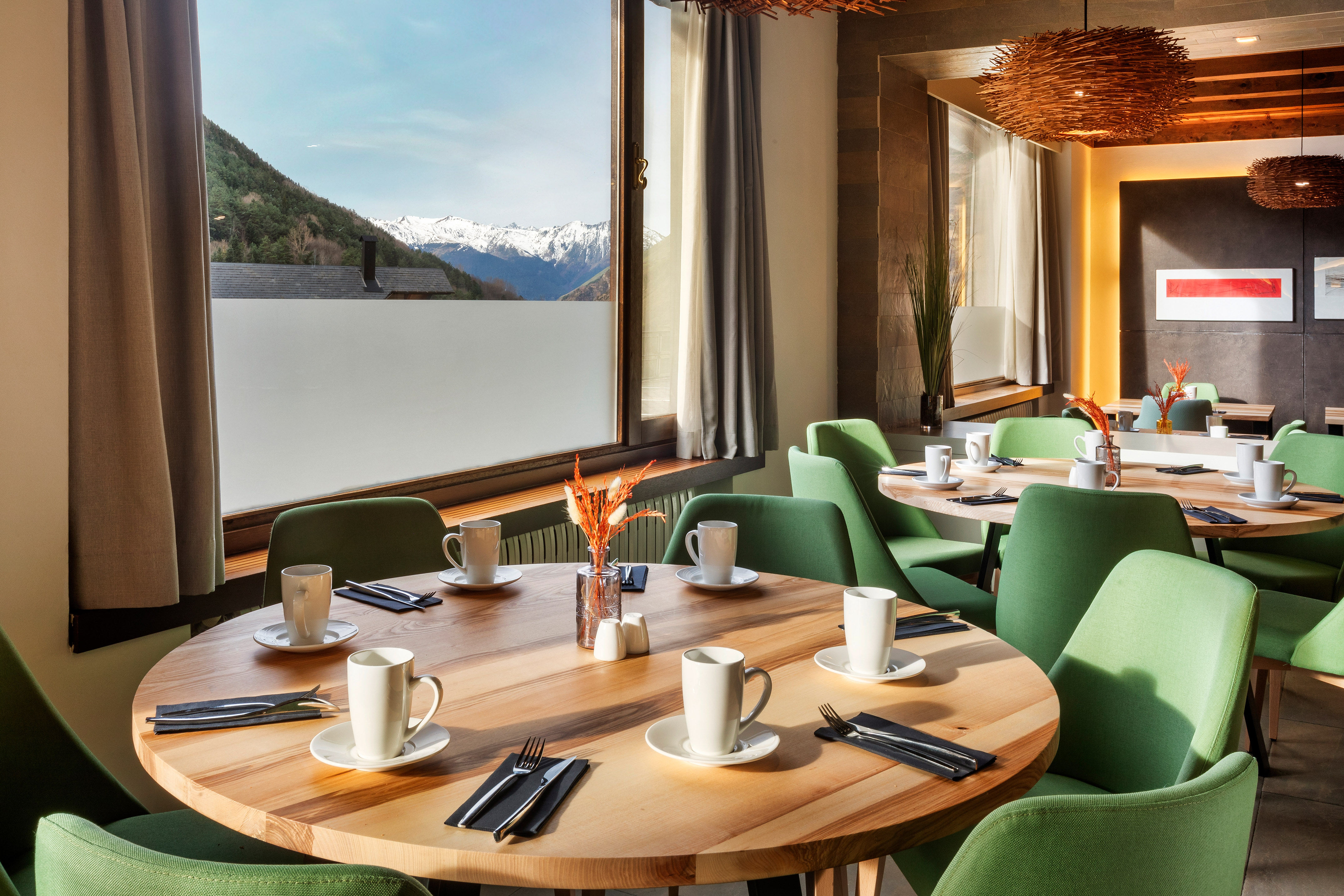 a table with white cups and green chairs in a room with a view of mountains