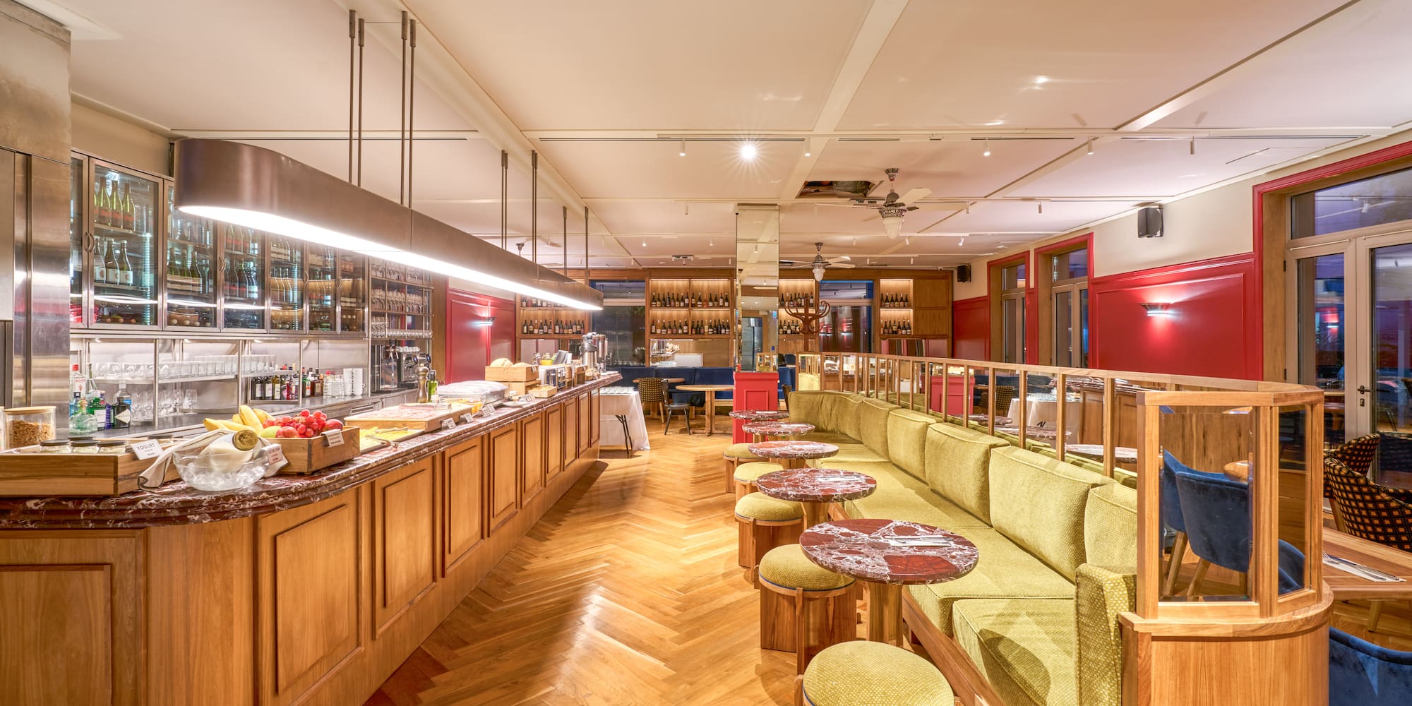 Restaurant interior: long bar, green banquette, red walls, herringbone floor.