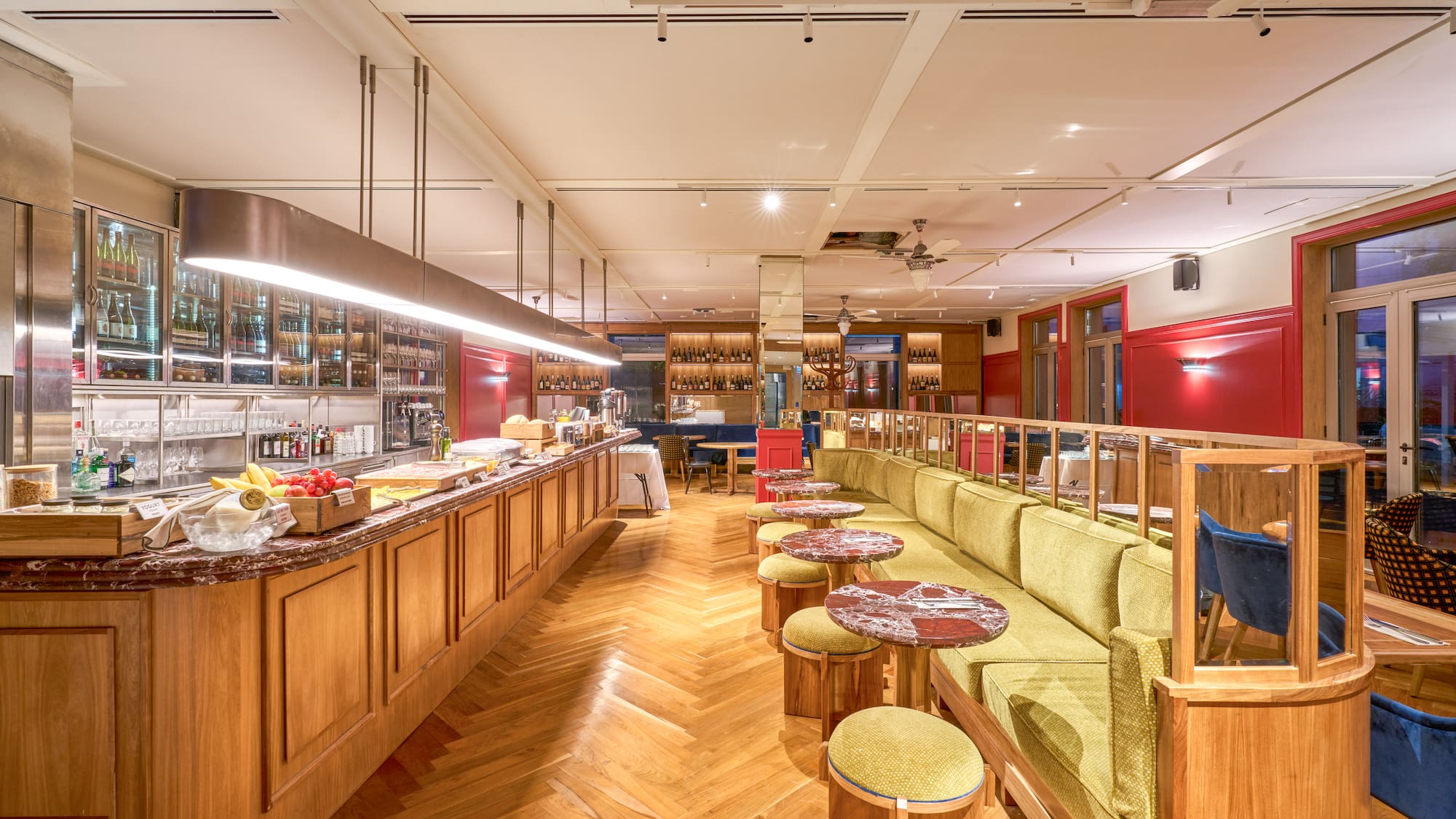 Restaurant interior: long bar, green banquette, red walls, herringbone floor.