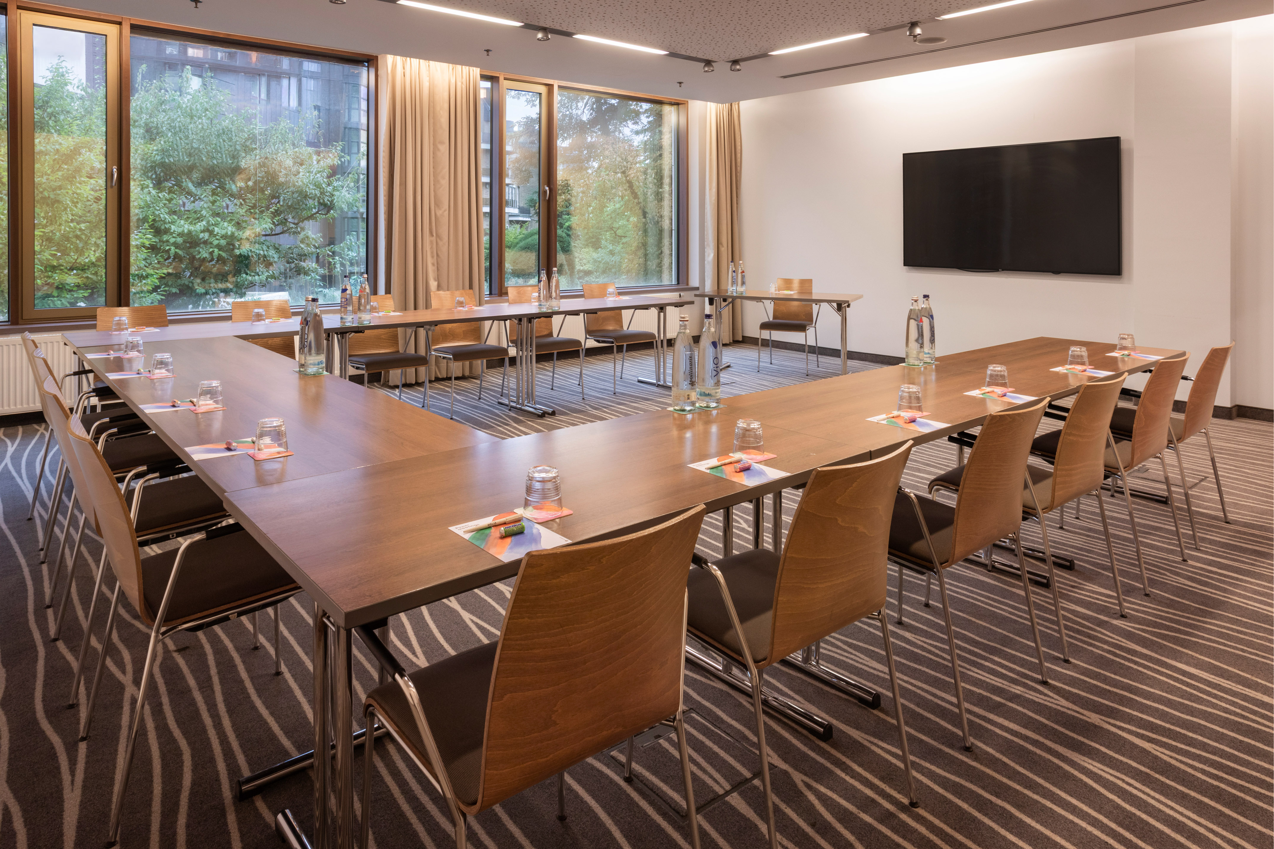 Modern U-shaped meeting room with large screen, tables, and outdoor views.