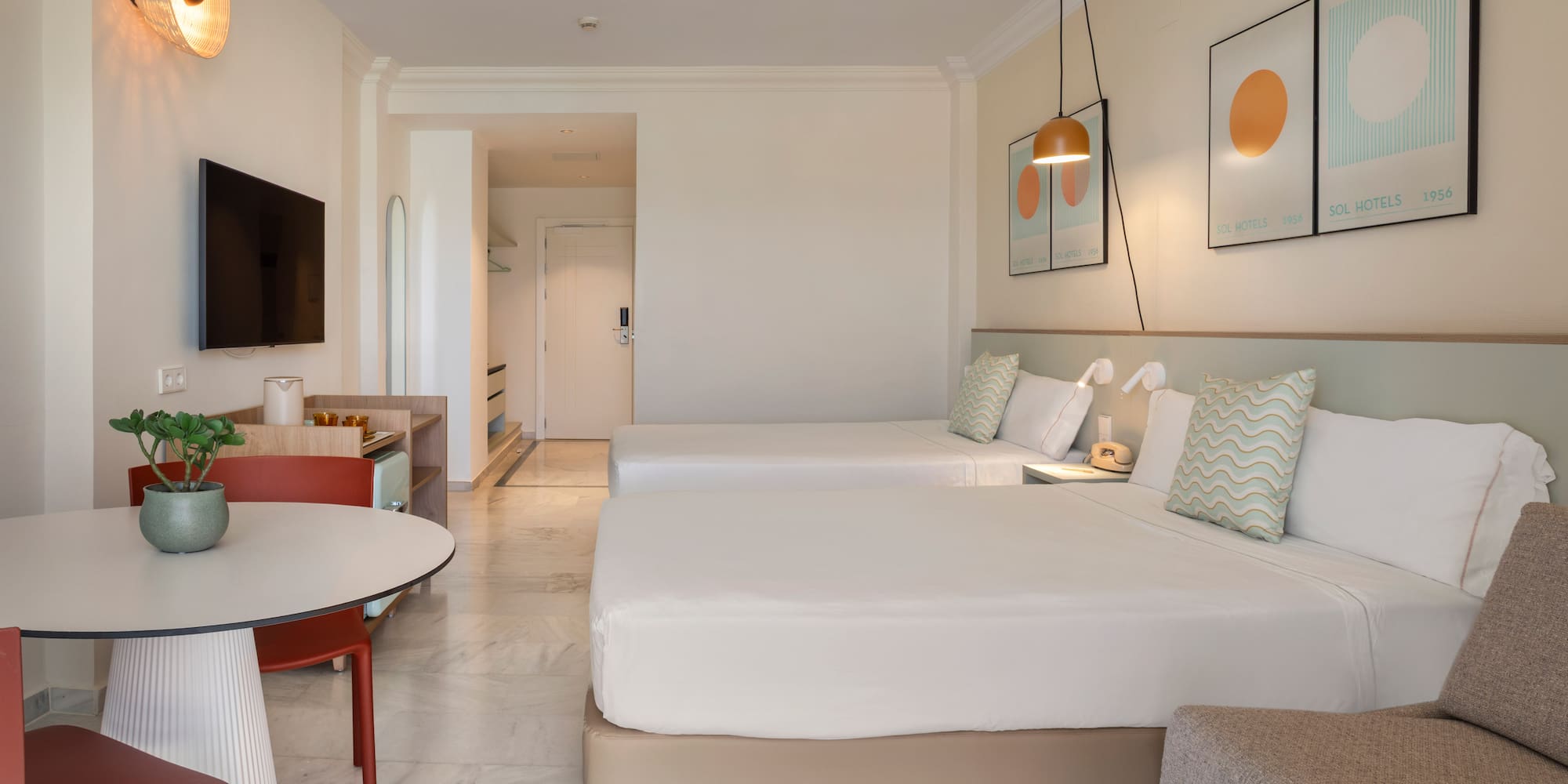 Modern hotel room with twin beds, dining area, and stylish decor.