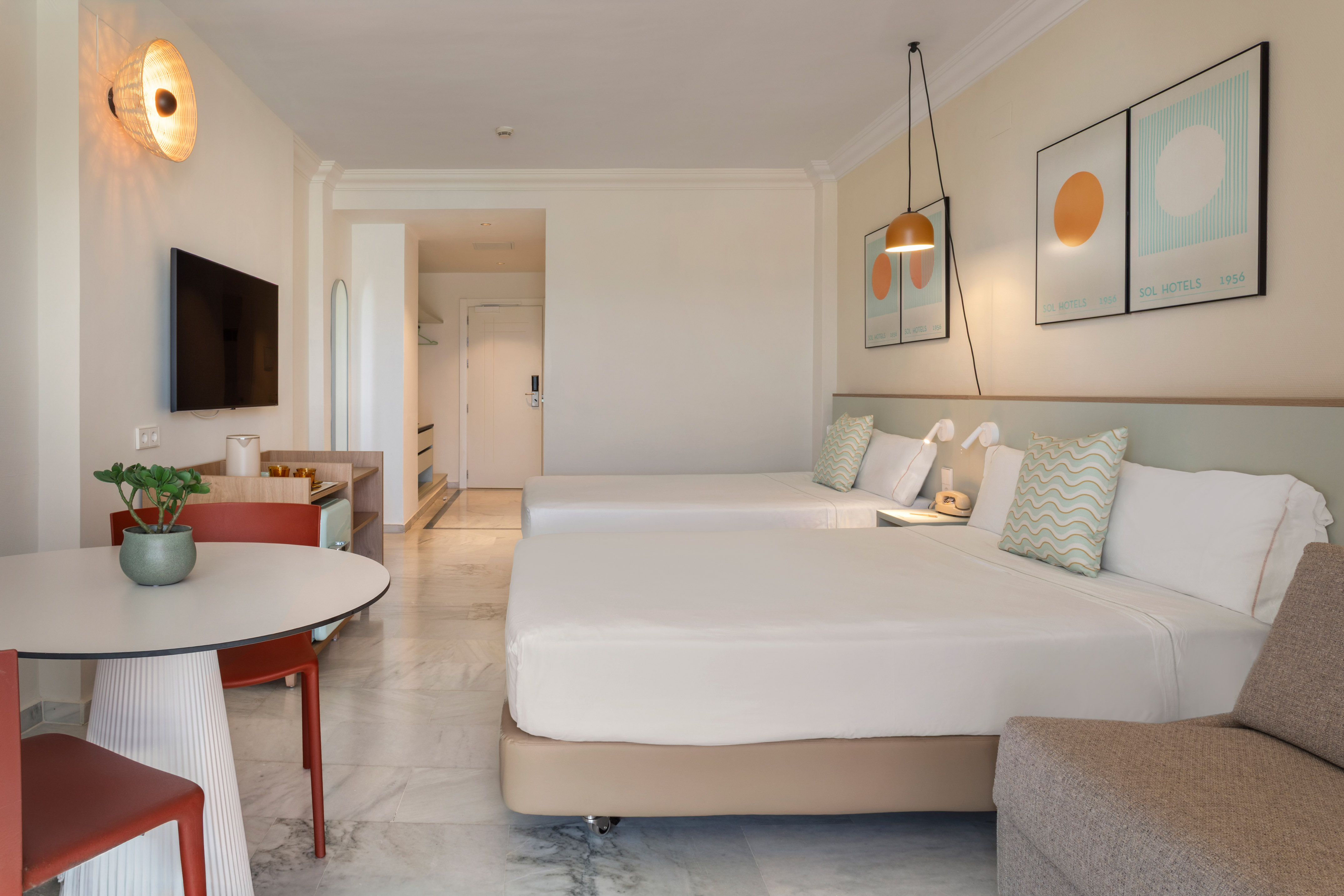 Modern hotel room with twin beds, dining area, and stylish decor.