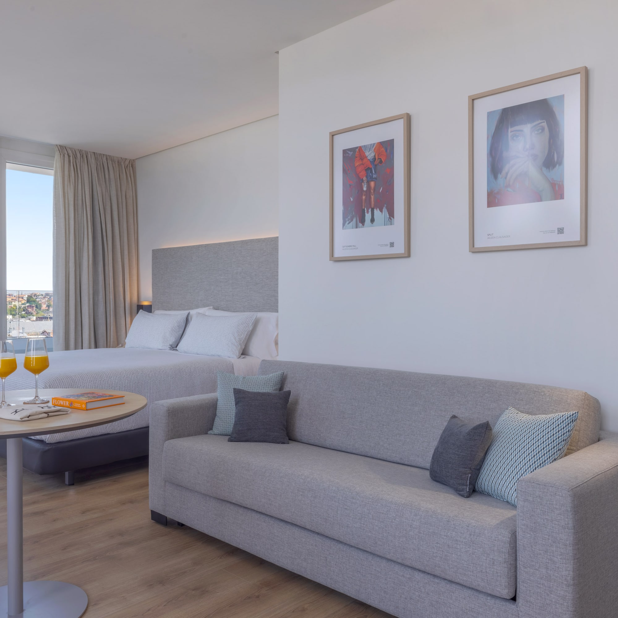 Suite hotelera moderna y luminosa con cama, sofá, y vista panorámica.