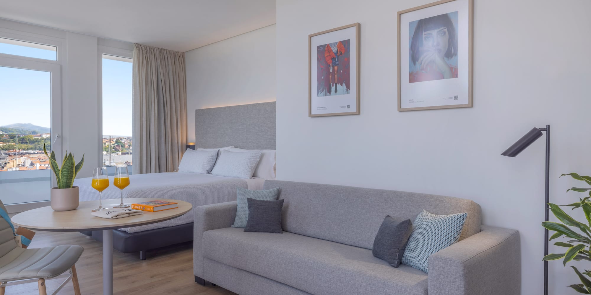 Suite hotelera moderna y luminosa con cama, sofá, y vista panorámica.