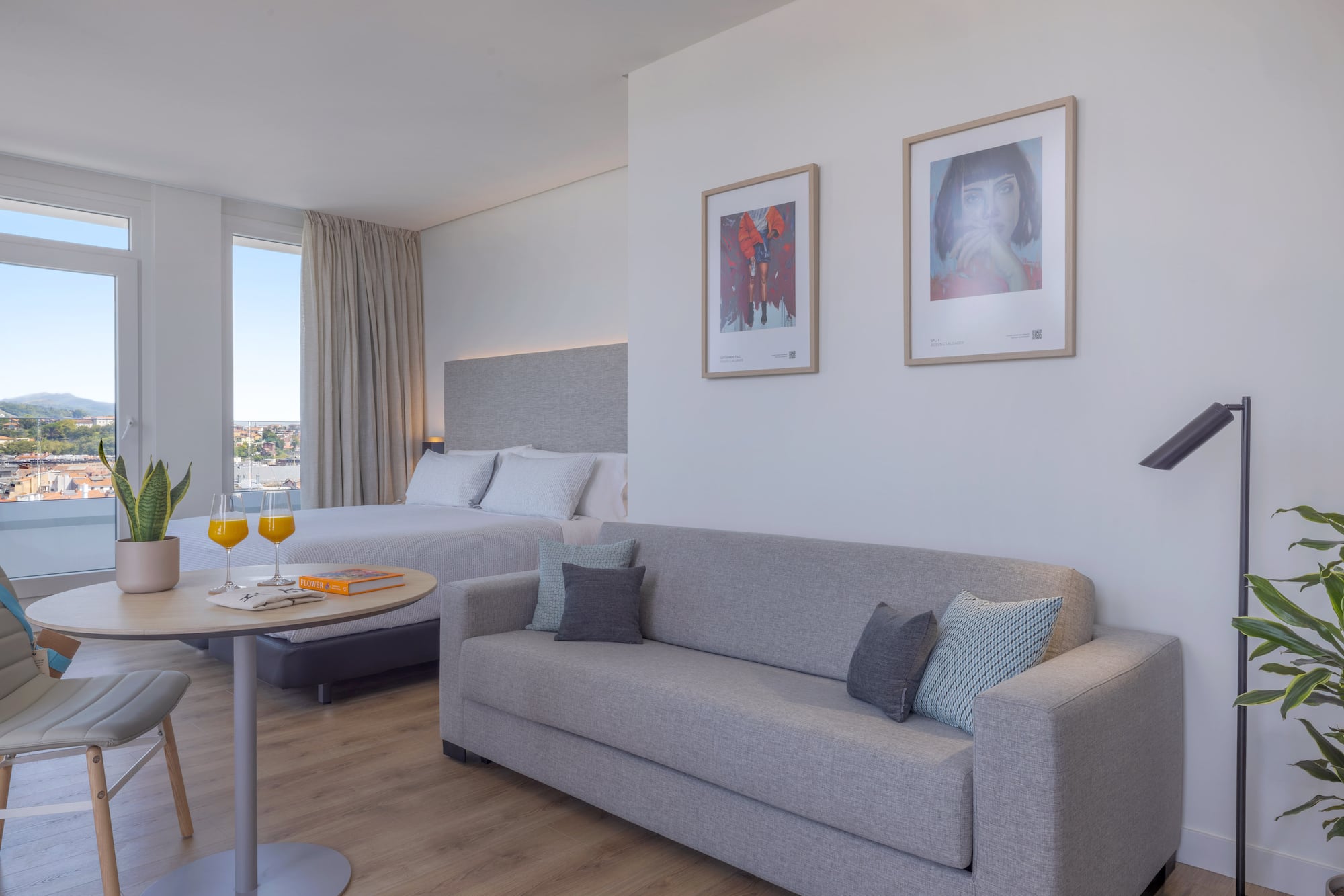 Suite hotelera moderna y luminosa con cama, sofá, y vista panorámica.