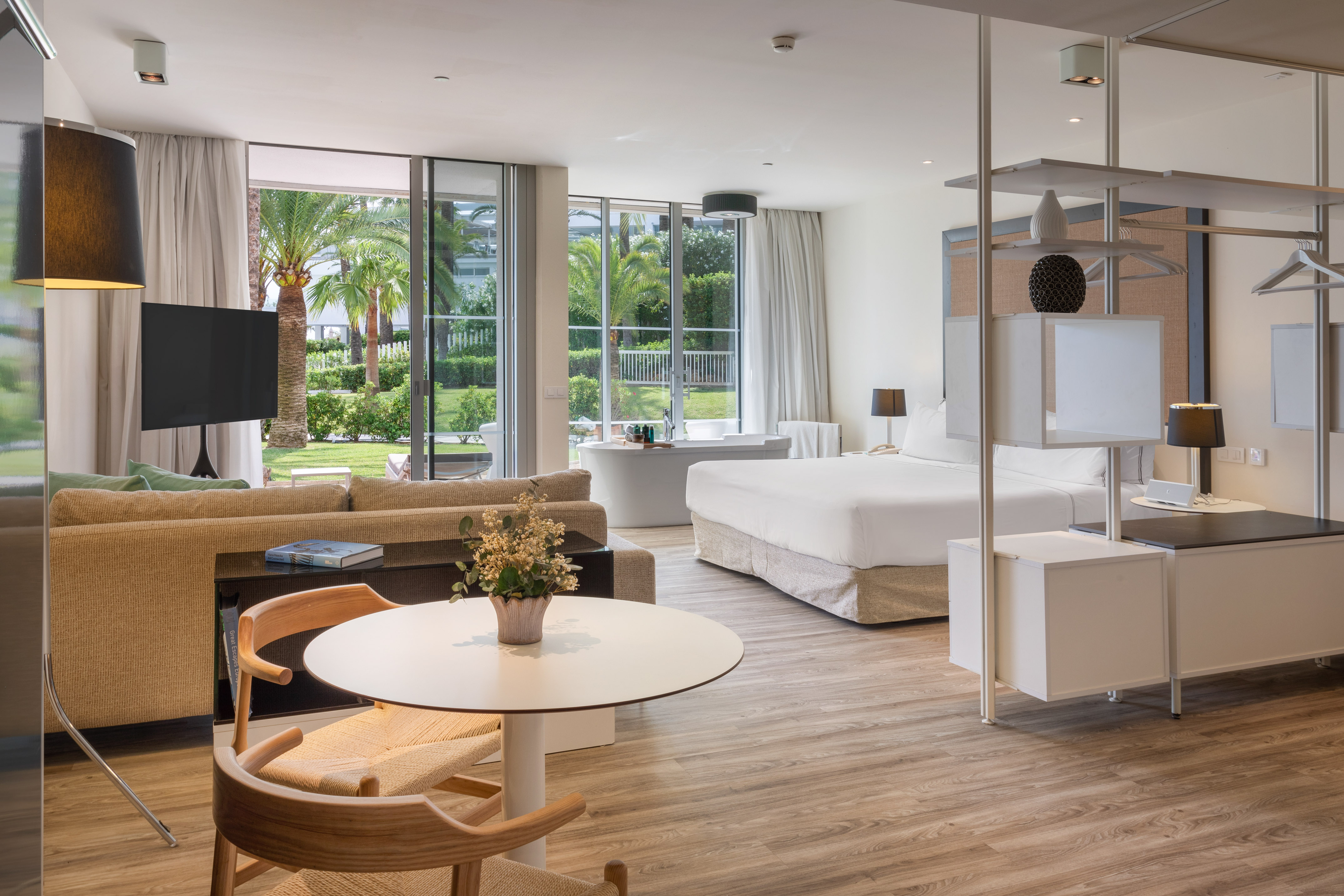 Luxury hotel suite with king bed, living area, bathtub, and tropical garden view.