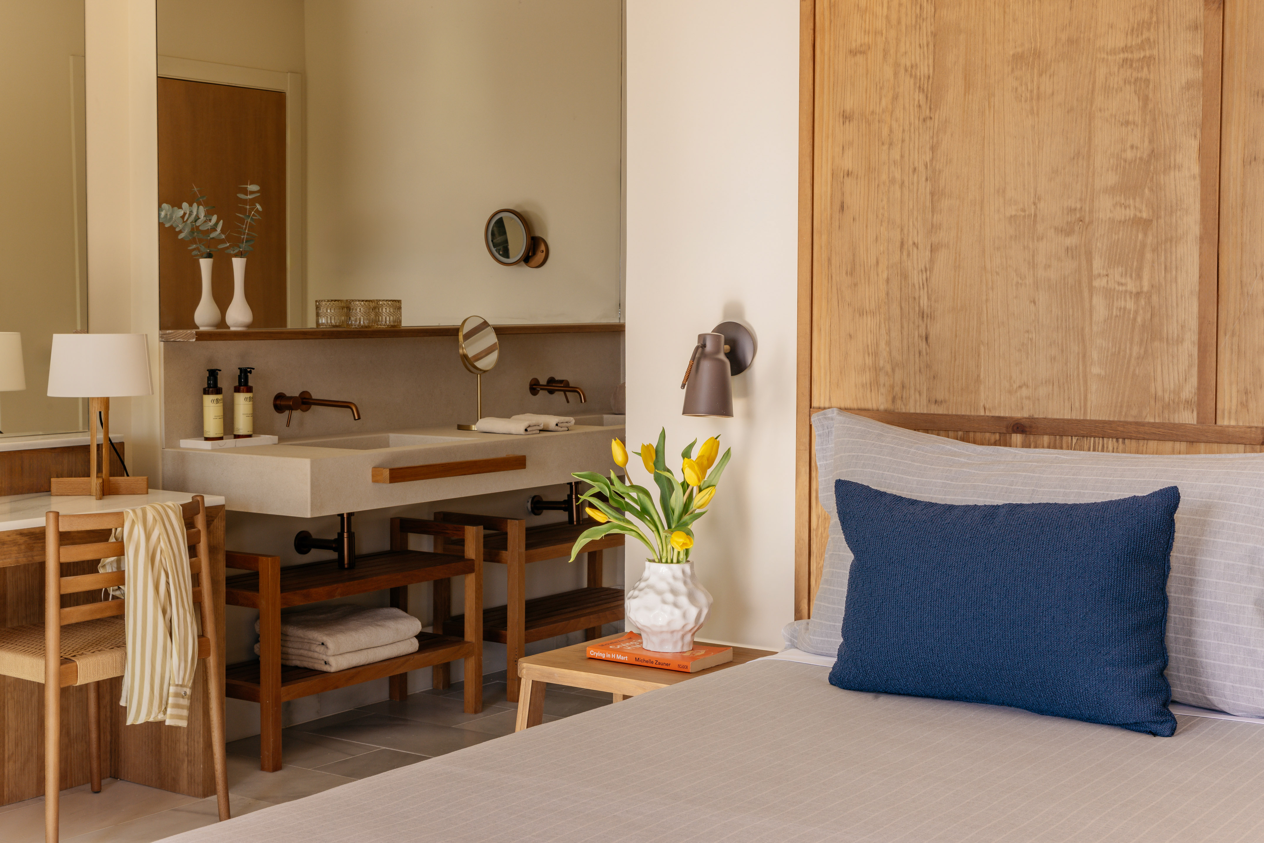 Modern hotel bedroom with wooden headboard, concrete vanity, and yellow tulips.