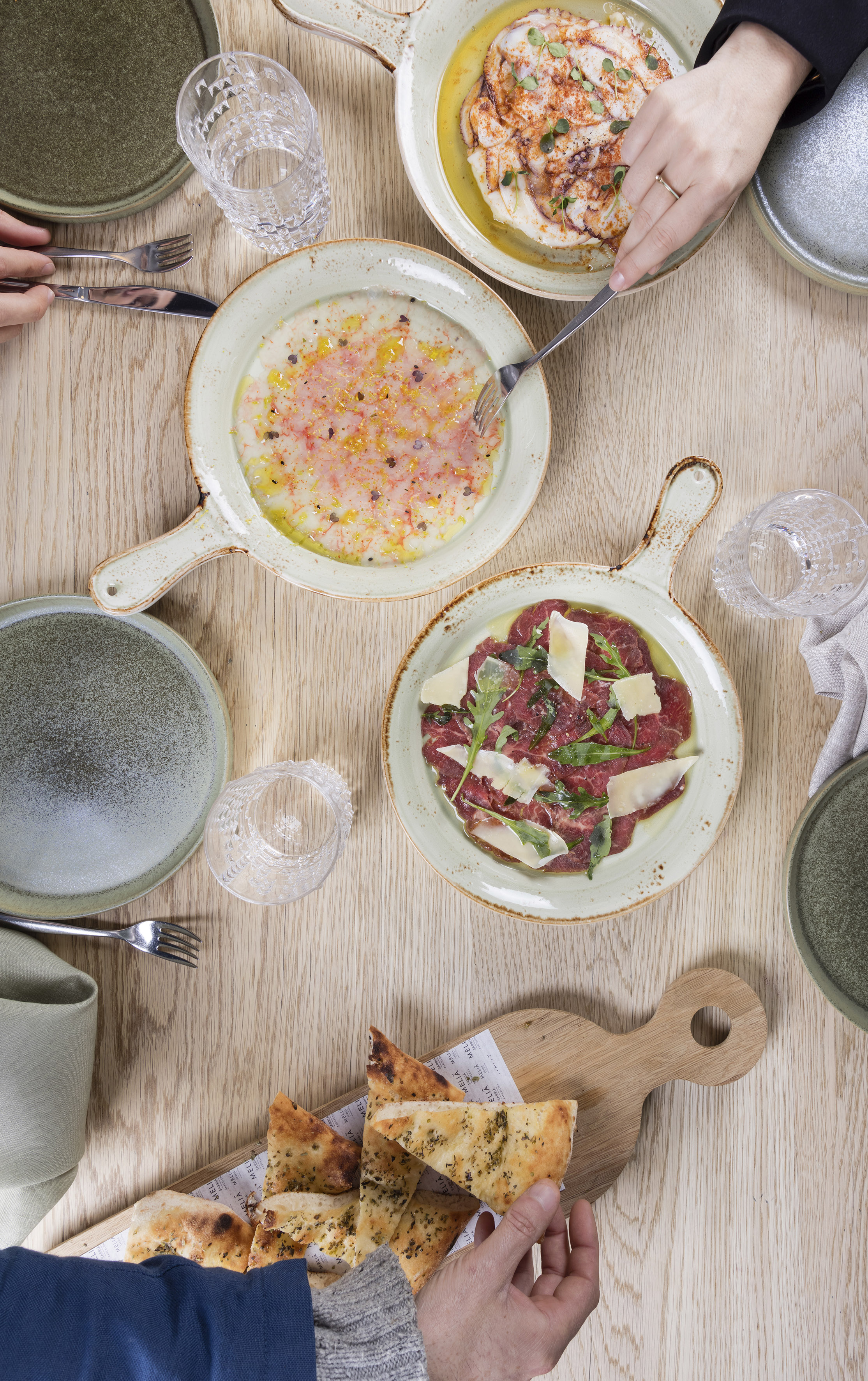 Octopus, seafood and beef carpaccio, focaccia, hands on dining table.