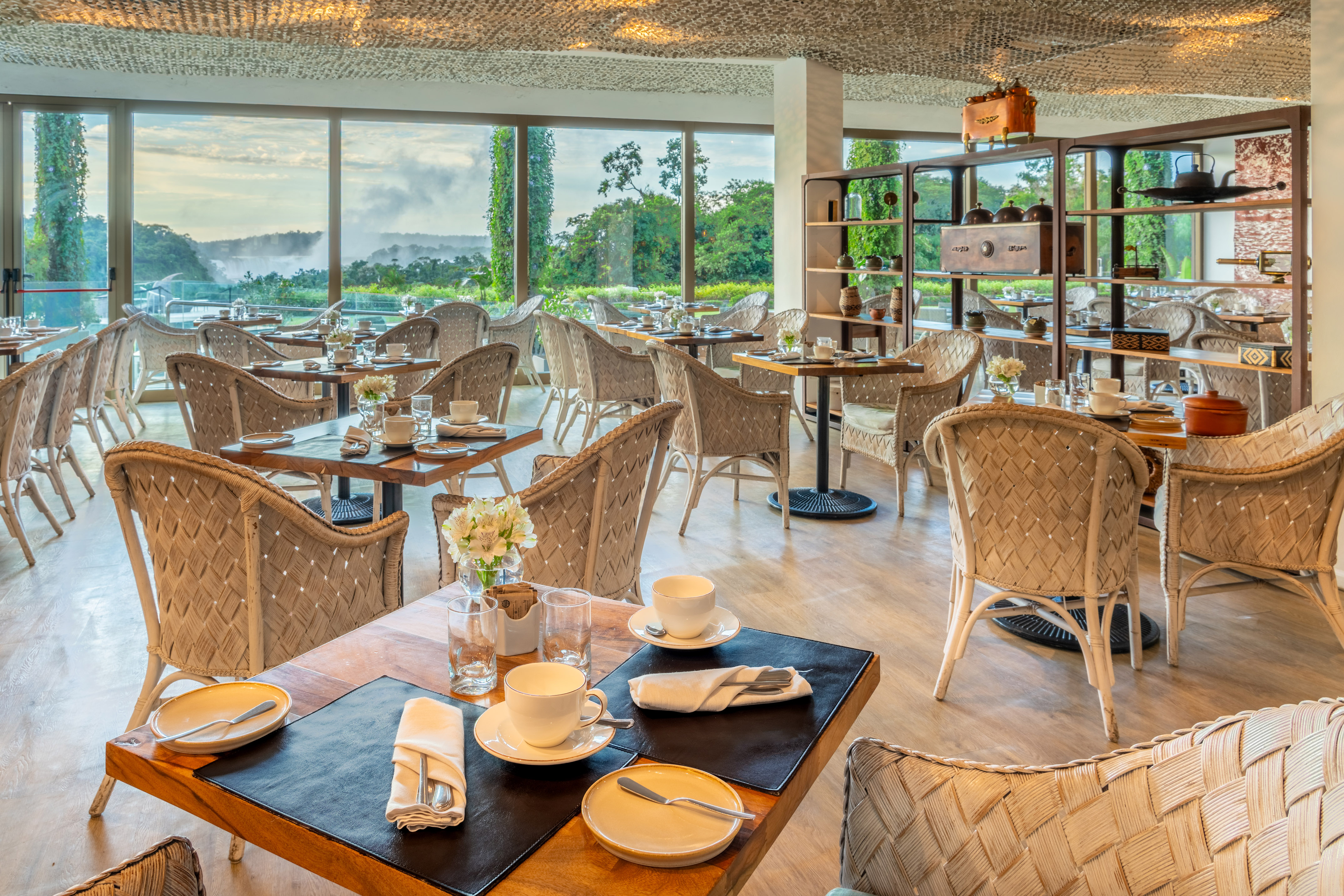 Luxury restaurant with rattan chairs, set tables, and Iguazu Falls view.