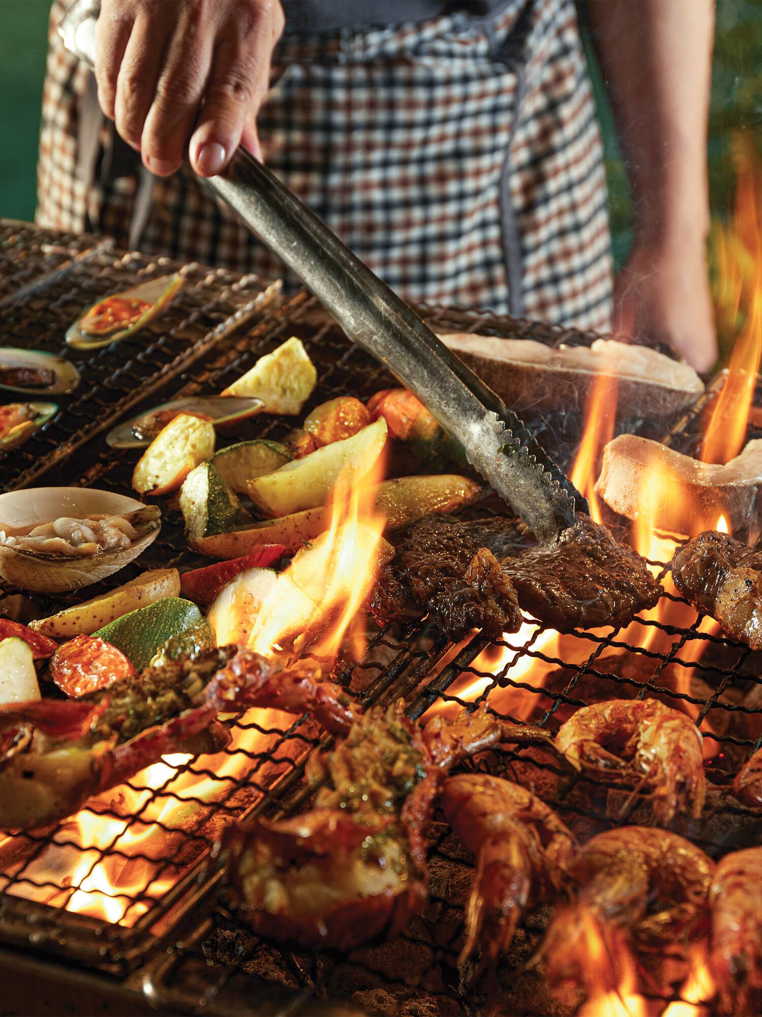 Outdoor BBQ with diverse seafood, meats, and vegetables grilling over flames.