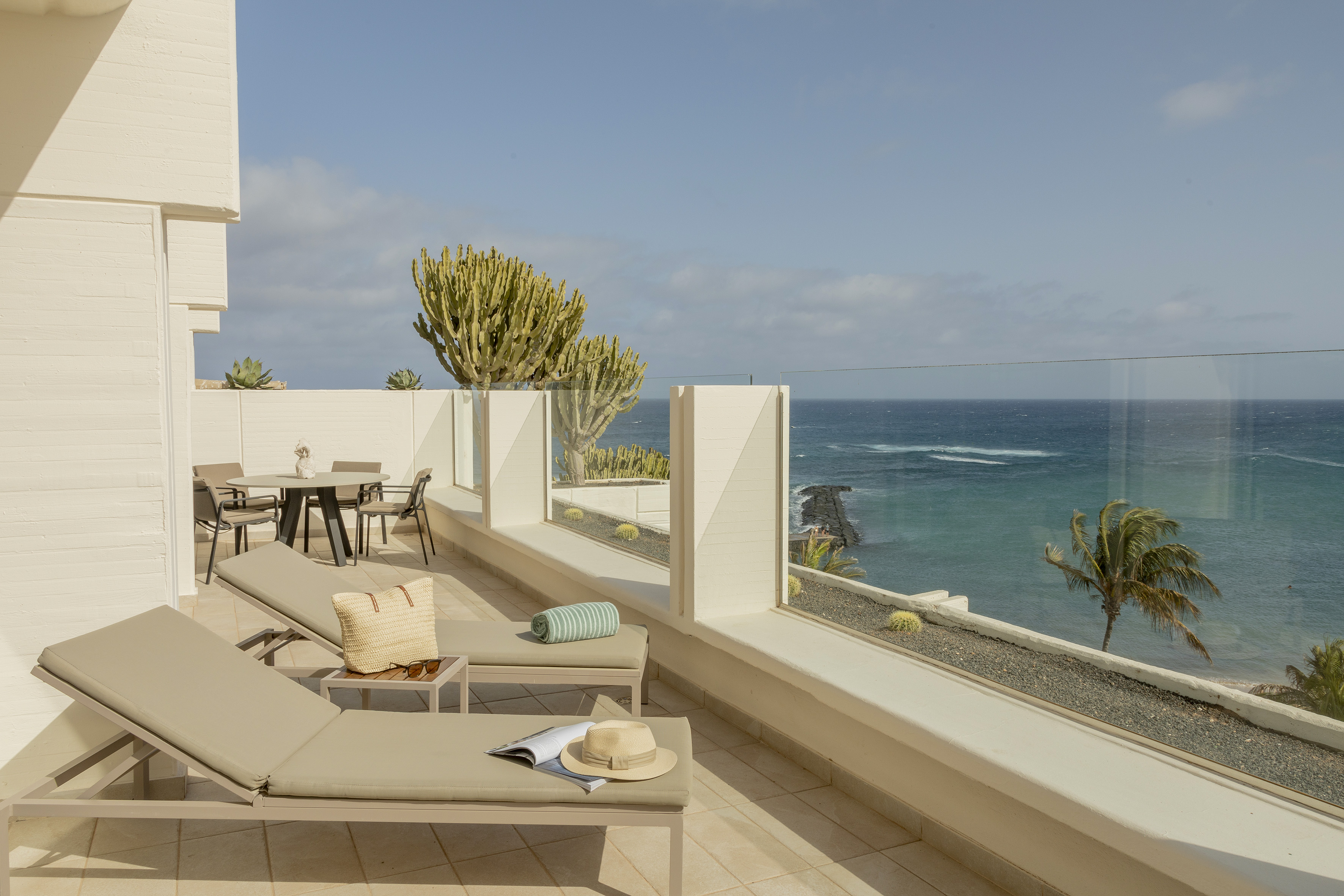 Coastal terrace with ocean view, sun loungers, outdoor dining, and cacti.