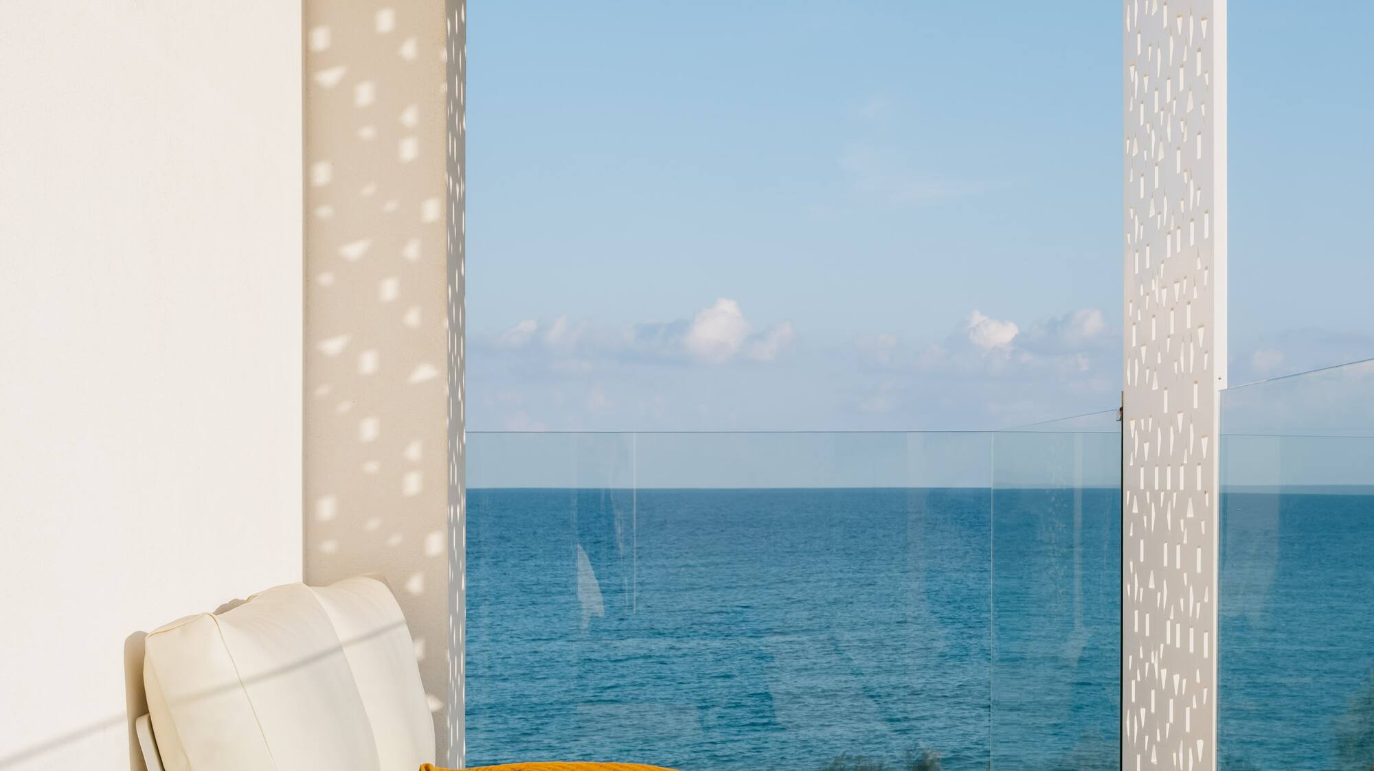 a white couch with a yellow blanket and a glass table with a view of the ocean