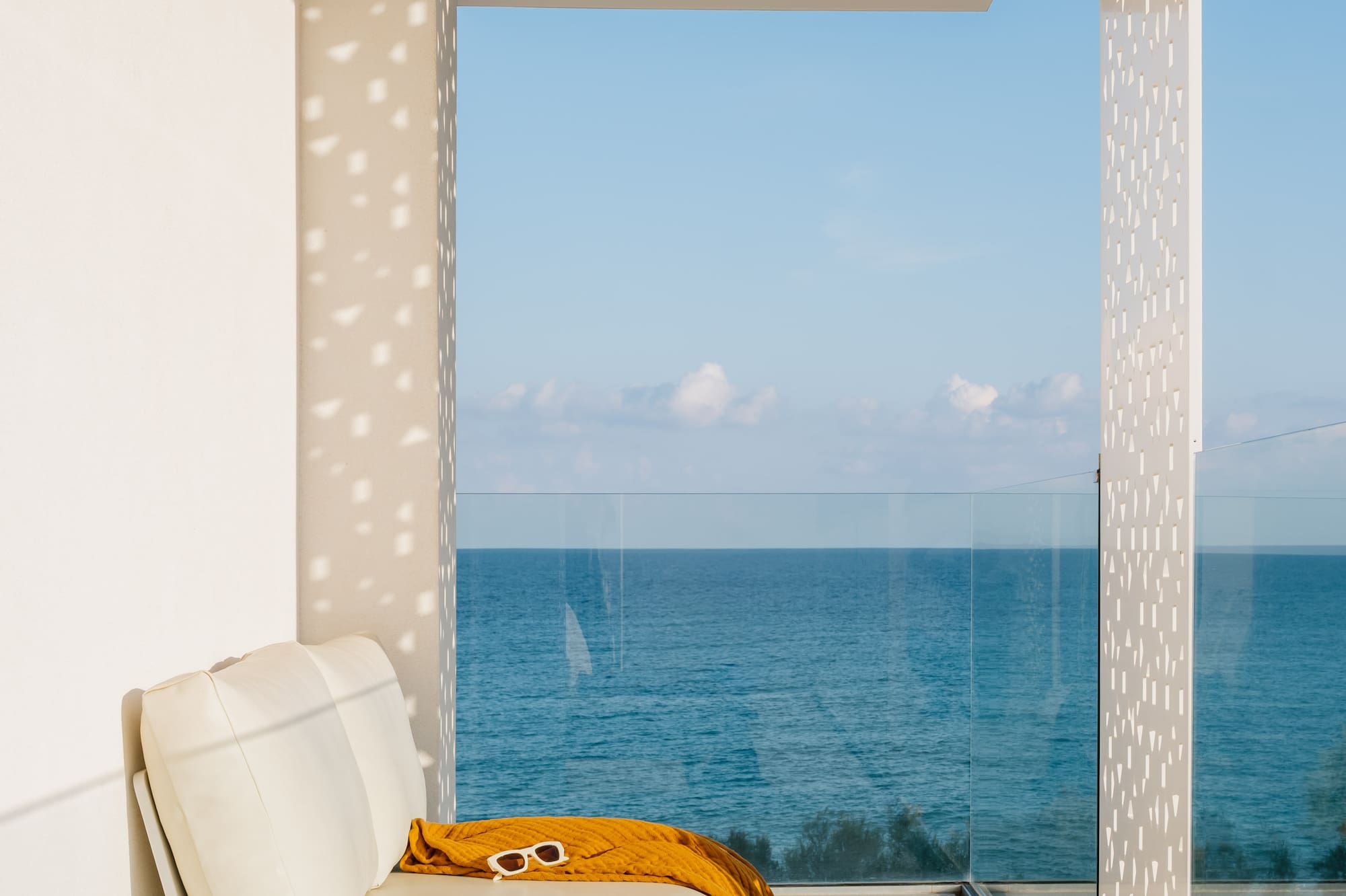a white couch with a yellow blanket and a glass table with a view of the ocean