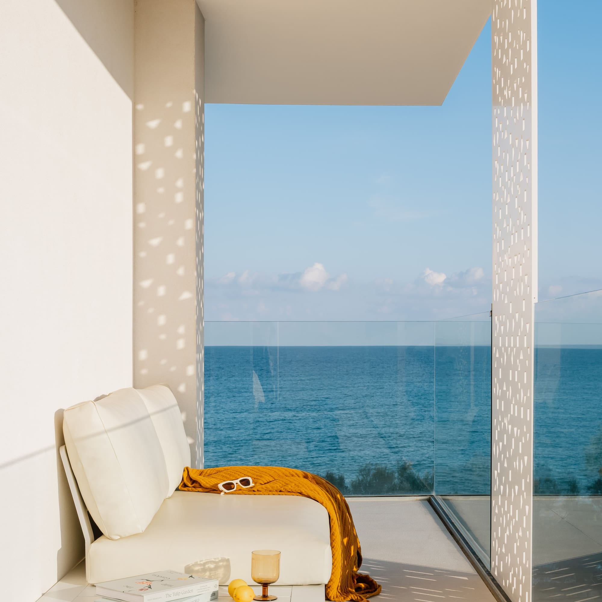 a white couch with a yellow blanket and a glass table with a view of the ocean