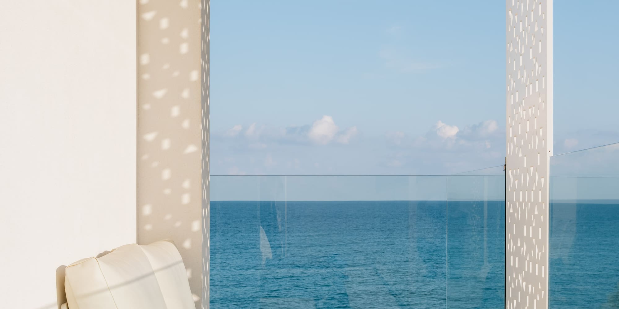 a white couch with a yellow blanket and a glass table with a view of the ocean