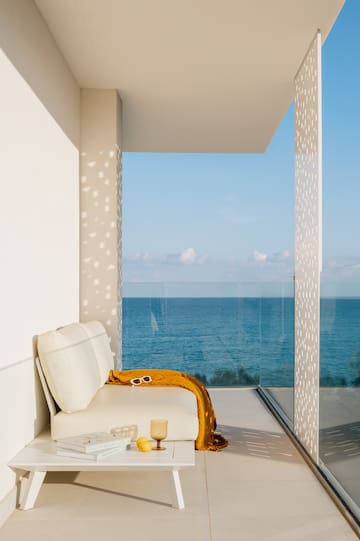 a white couch with a yellow blanket and a glass table with a view of the ocean