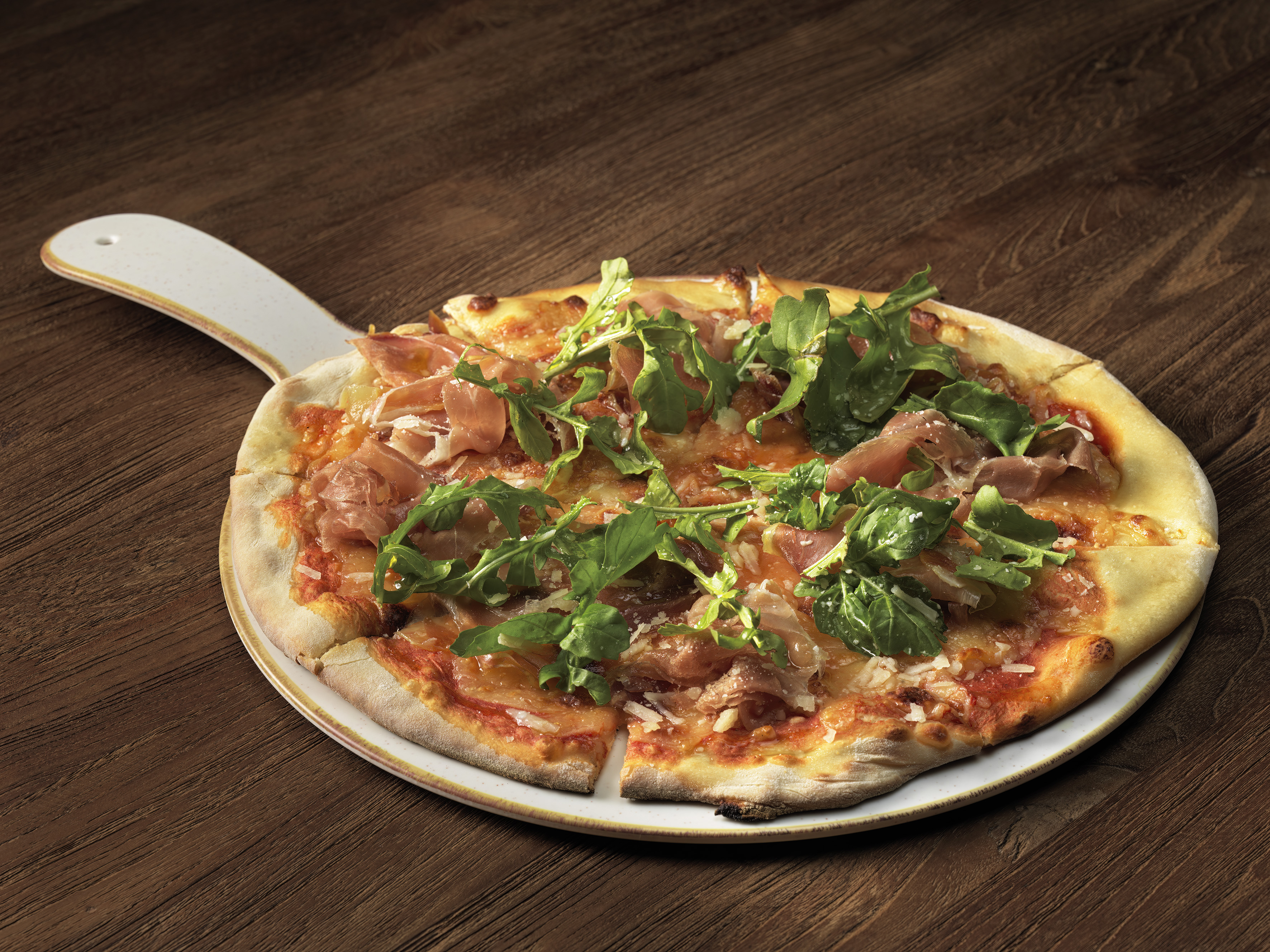 Prosciutto and arugula pizza with parmesan on a white pizza peel.