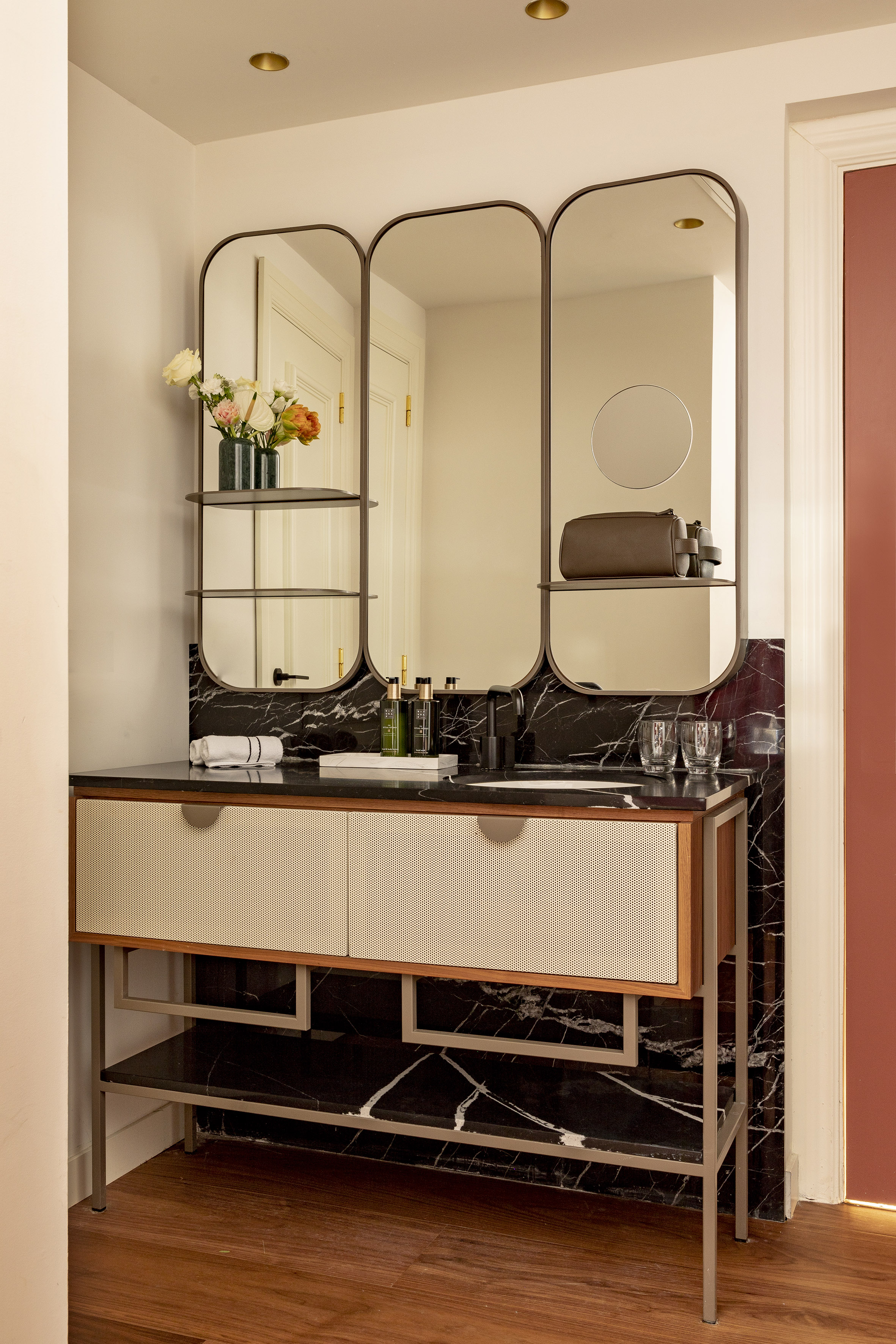 Modern black marble bathroom vanity with sink and three arched mirrors.