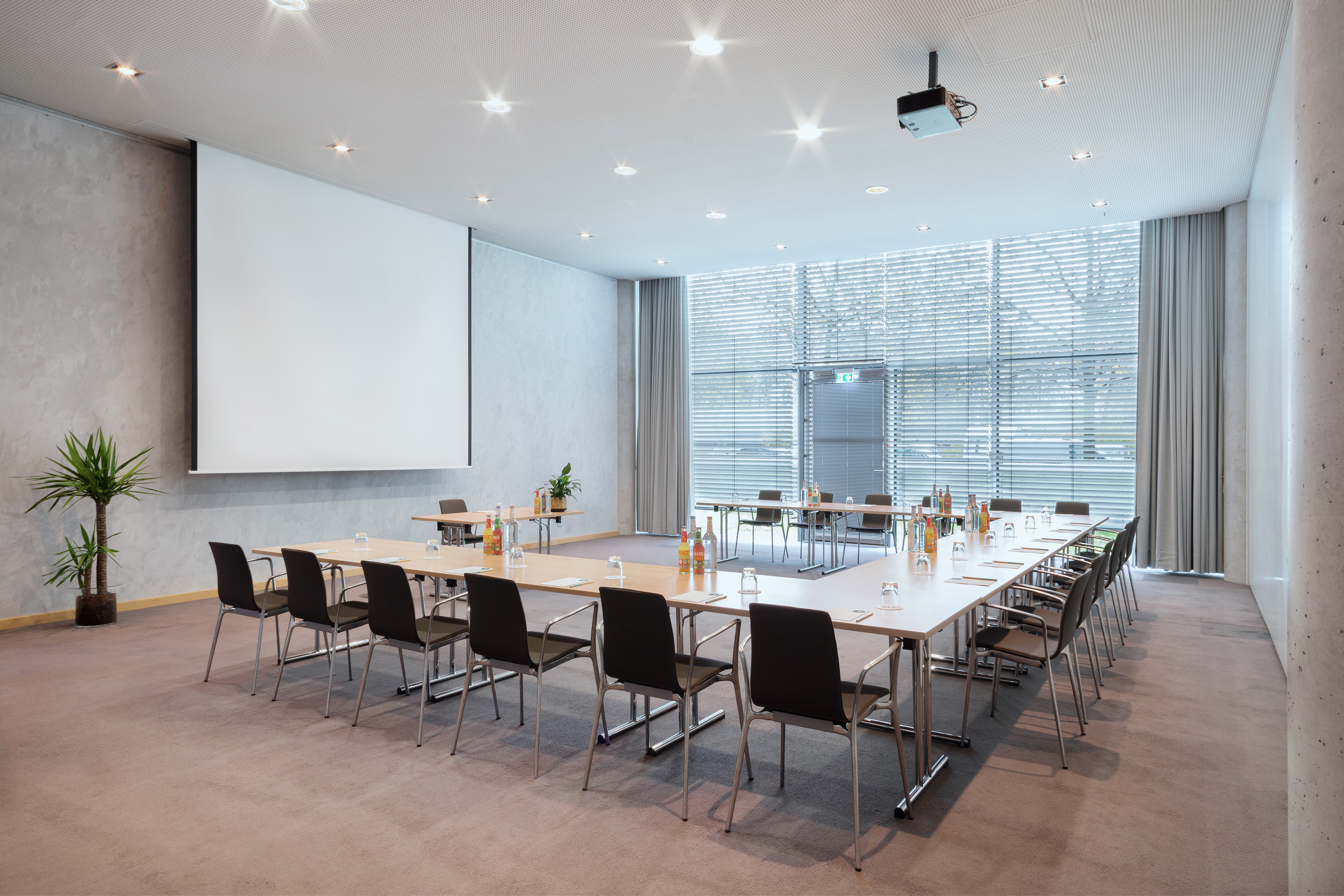 Empty modern meeting room, U-shaped table, projector, large windows.