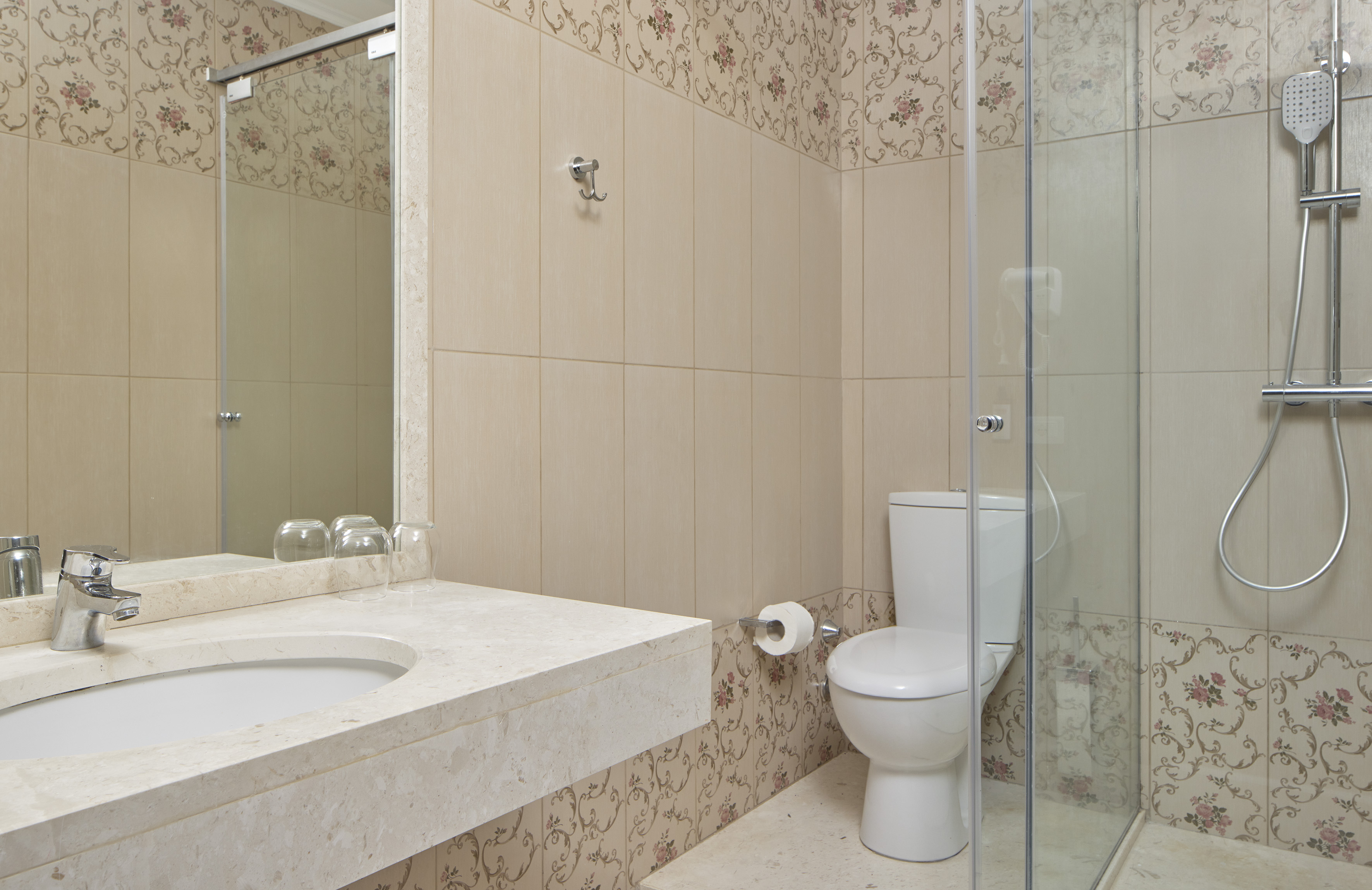 Bathroom with vanity, toilet, glass shower, and floral beige wall tiles.