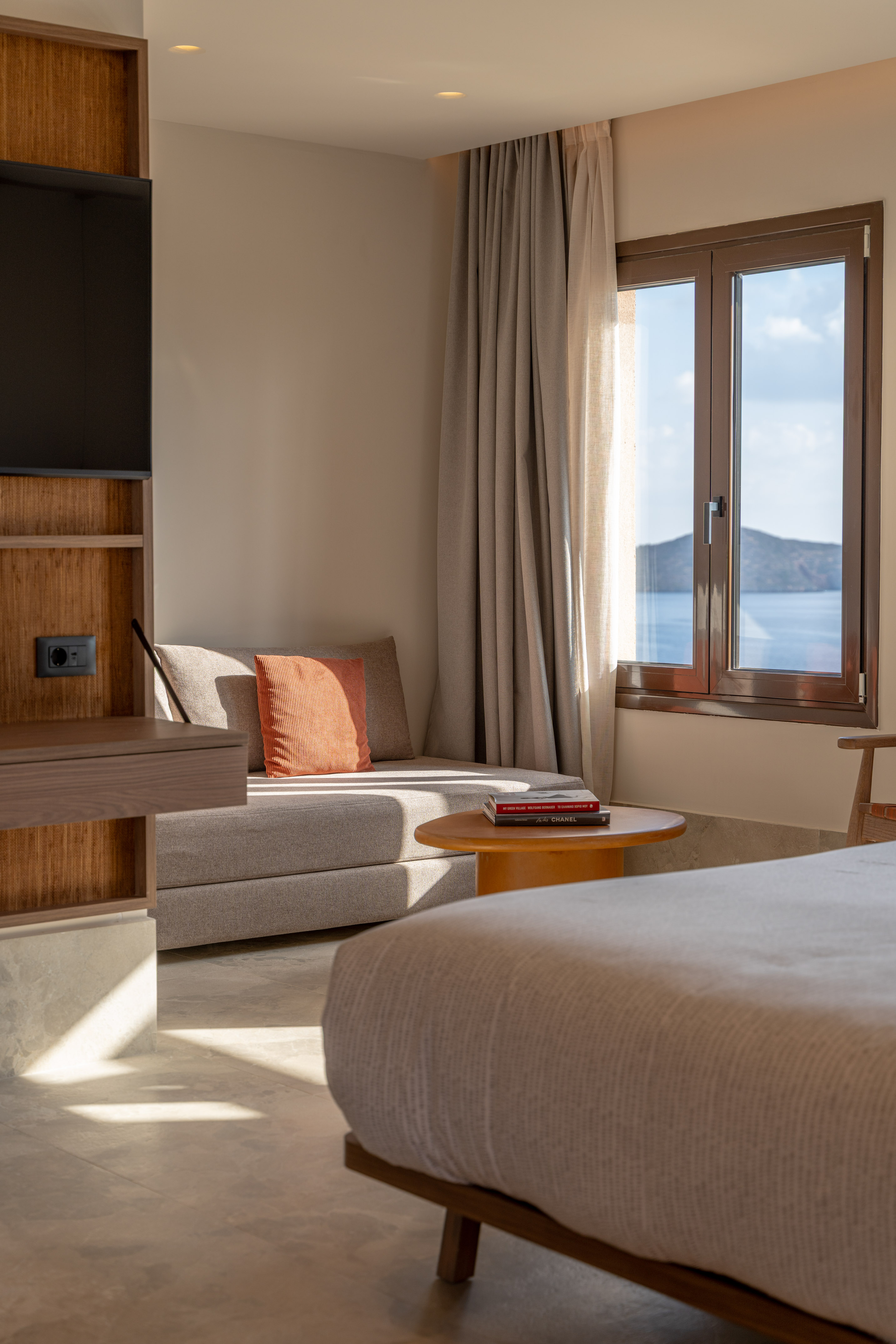 Modern hotel room with sea view, sunlit lounge area, and warm wooden accents.