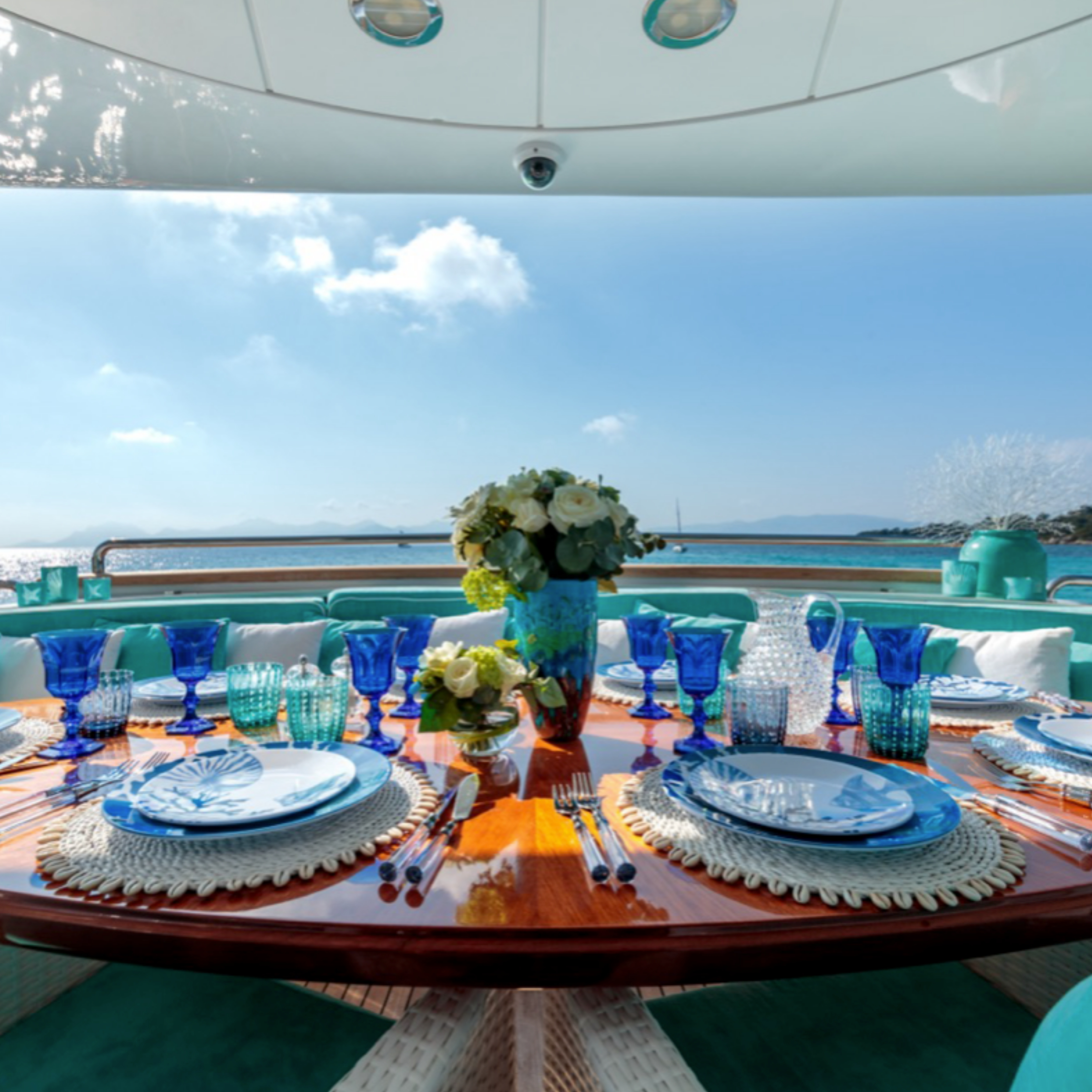 Elegant yacht dining table set with blue dinnerware, flowers, and sea view.
