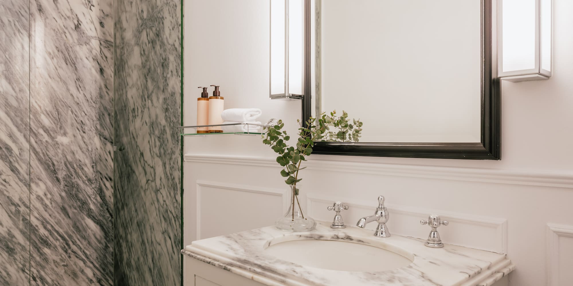 Luxury bathroom with white marble vanity, chrome fixtures, modern mirror, and shower.
