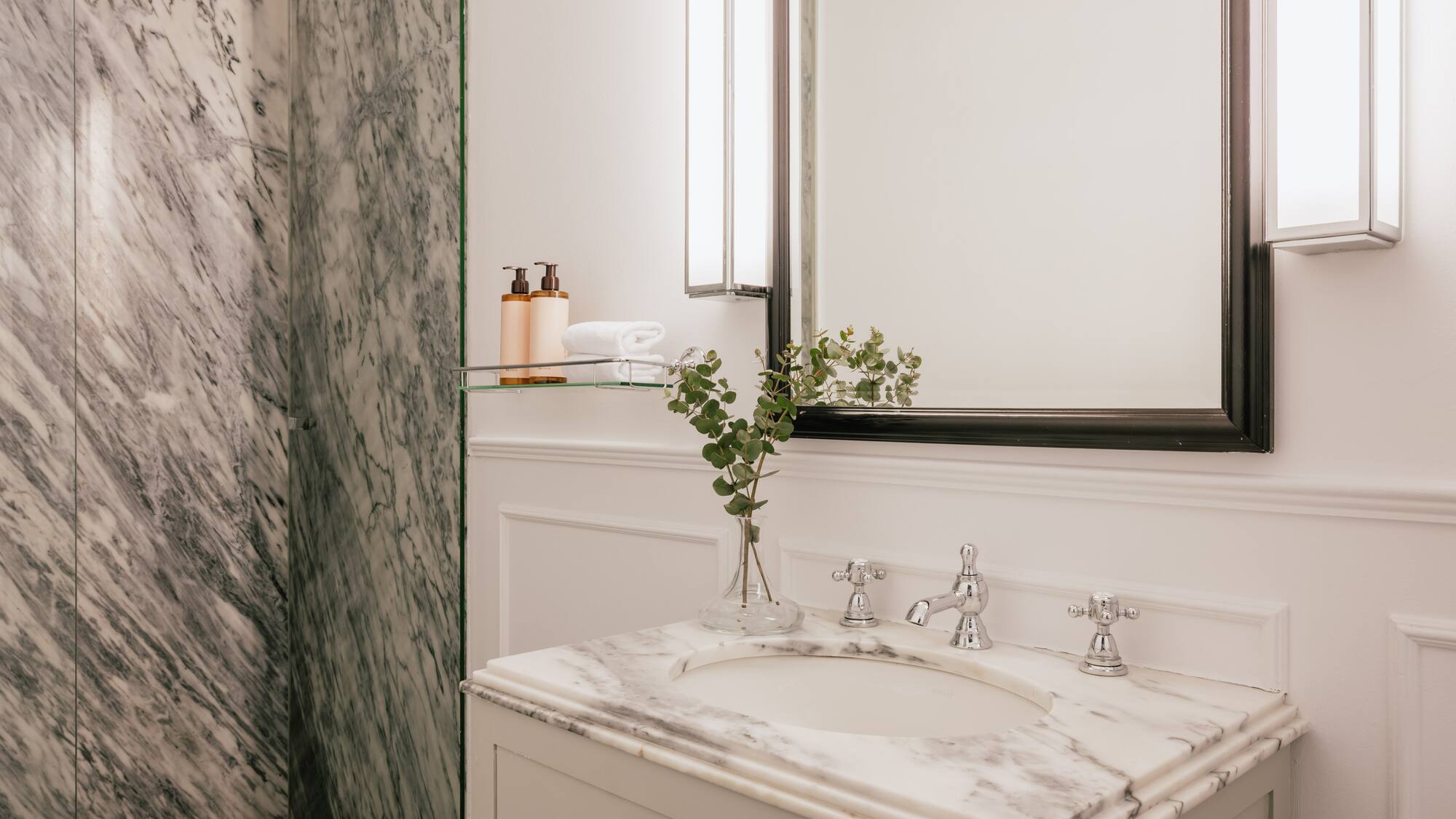 Elegant bathroom with marble vanity, chrome fixtures, mirror, and white wainscoting.