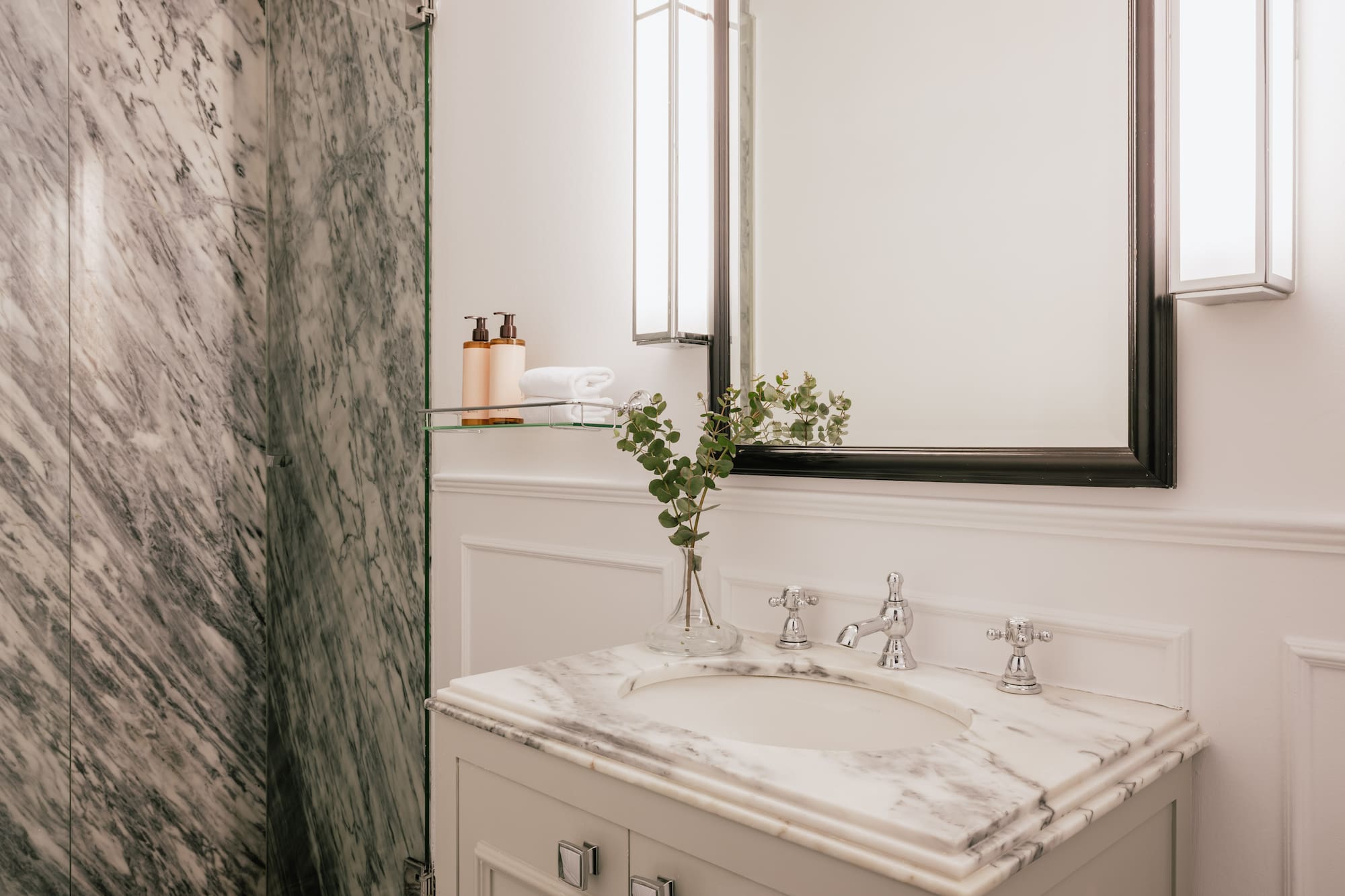 Luxury bathroom with white marble vanity, chrome fixtures, modern mirror, and shower.