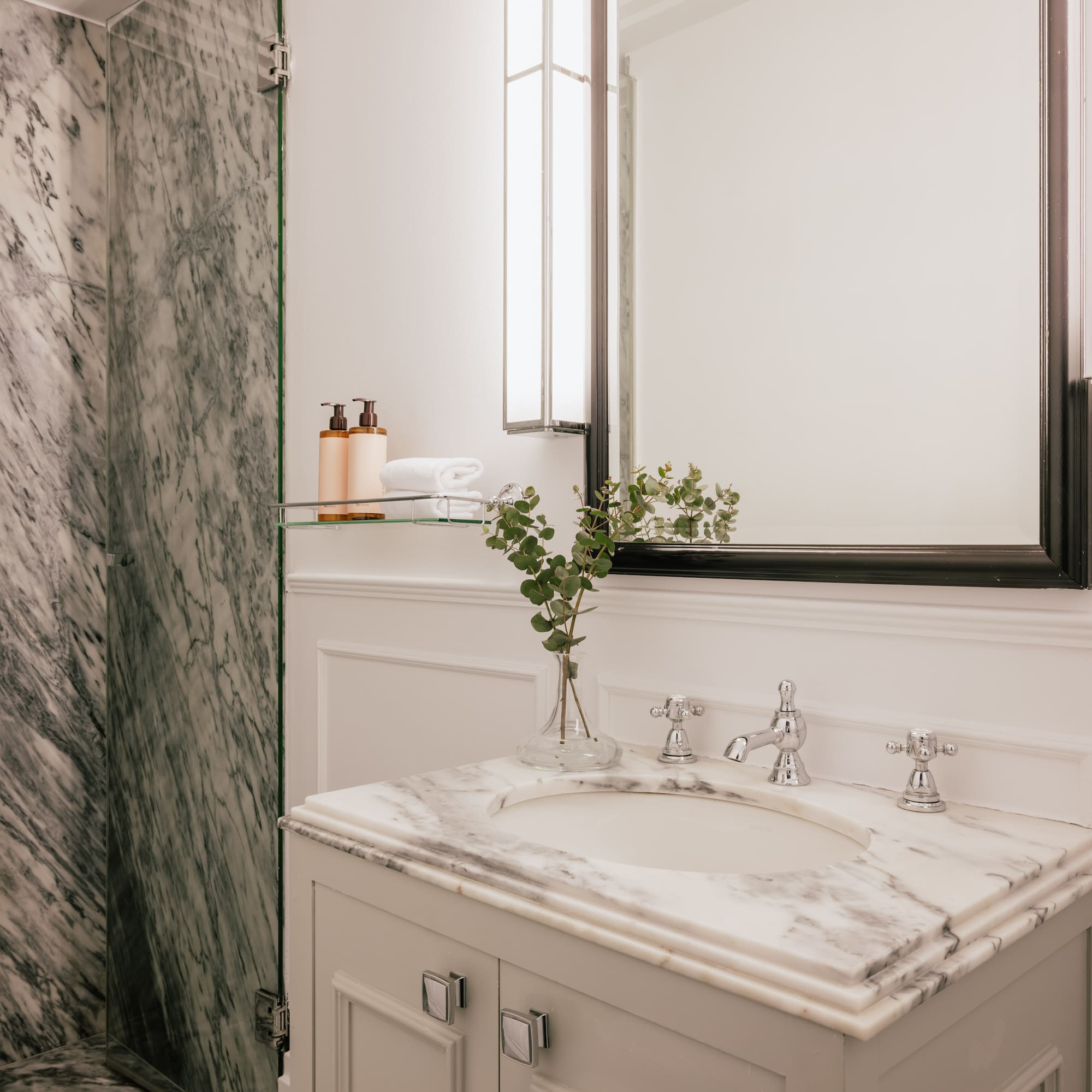 Luxury bathroom with white marble vanity, chrome fixtures, modern mirror, and shower.