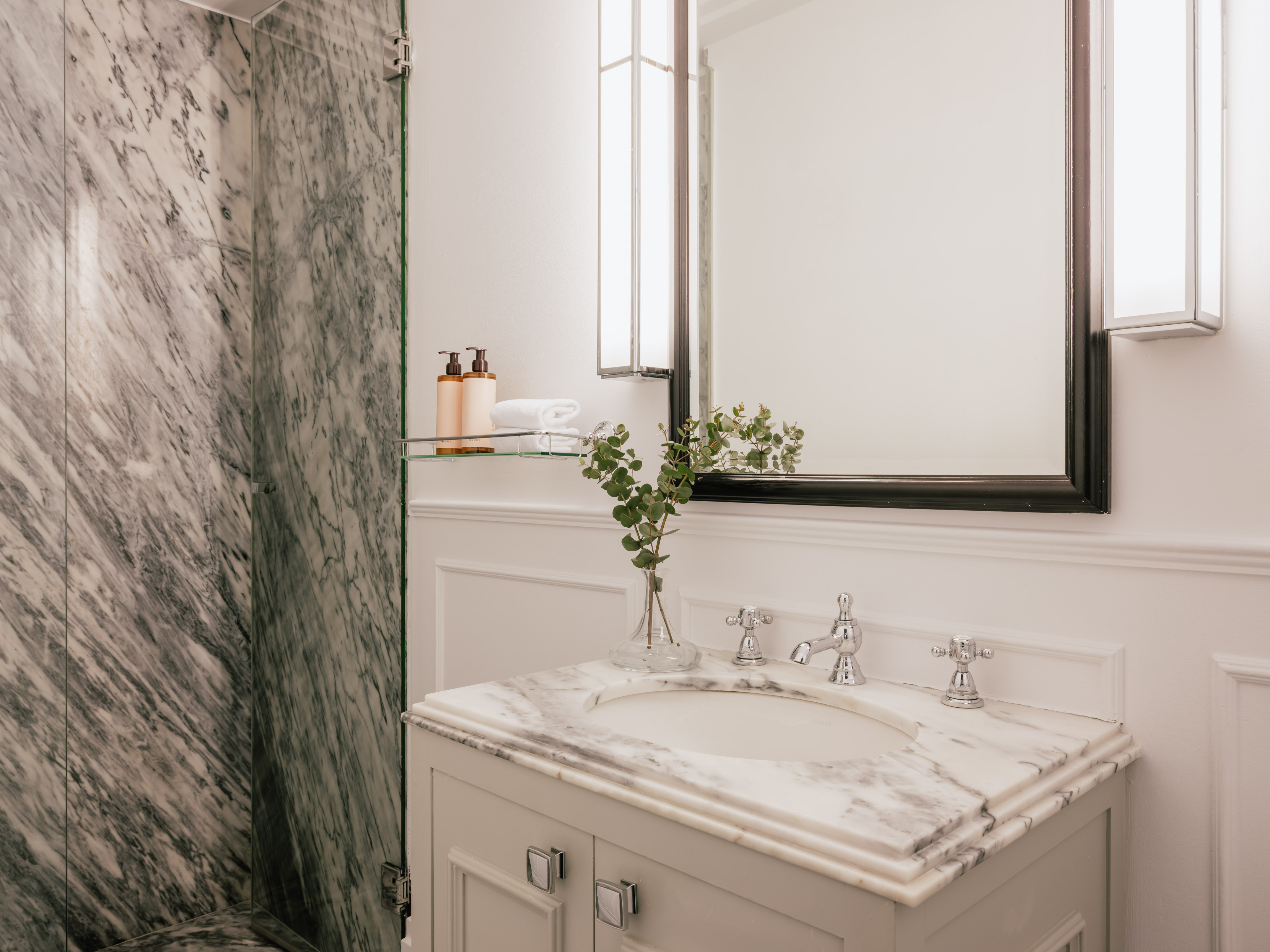 Luxury bathroom with white marble vanity, chrome fixtures, modern mirror, and shower.