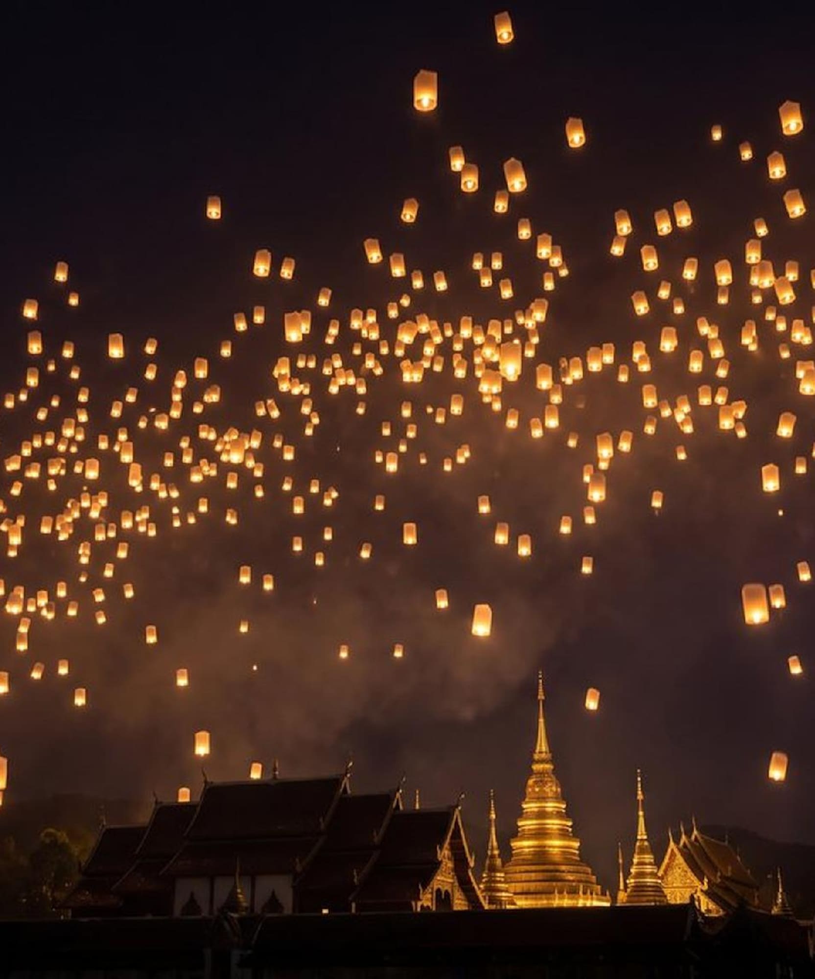 Glowing sky lanterns fill the night sky above a golden temple.