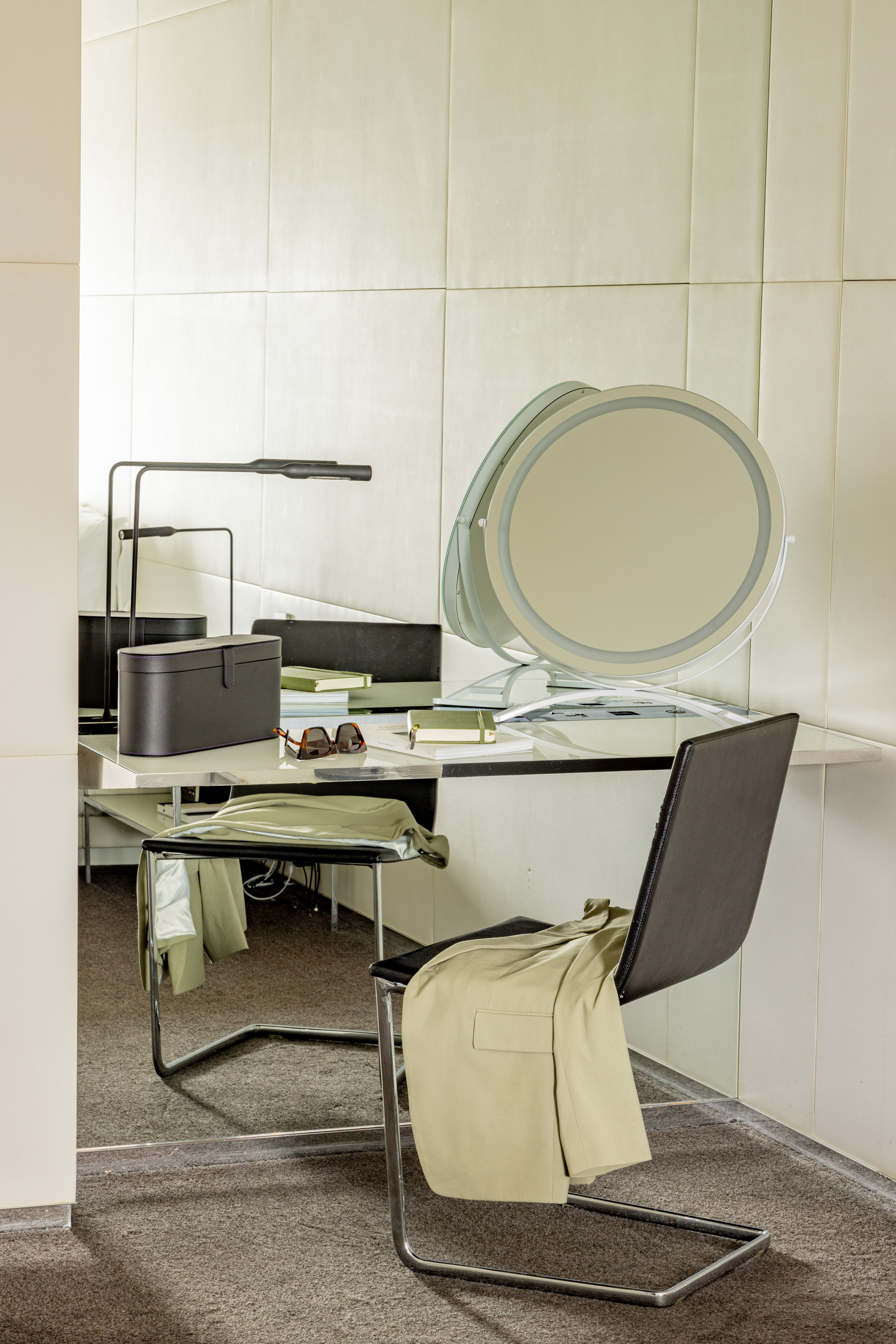 Neutral modern dressing table with a lighted mirror, lamp, and draped jacket.