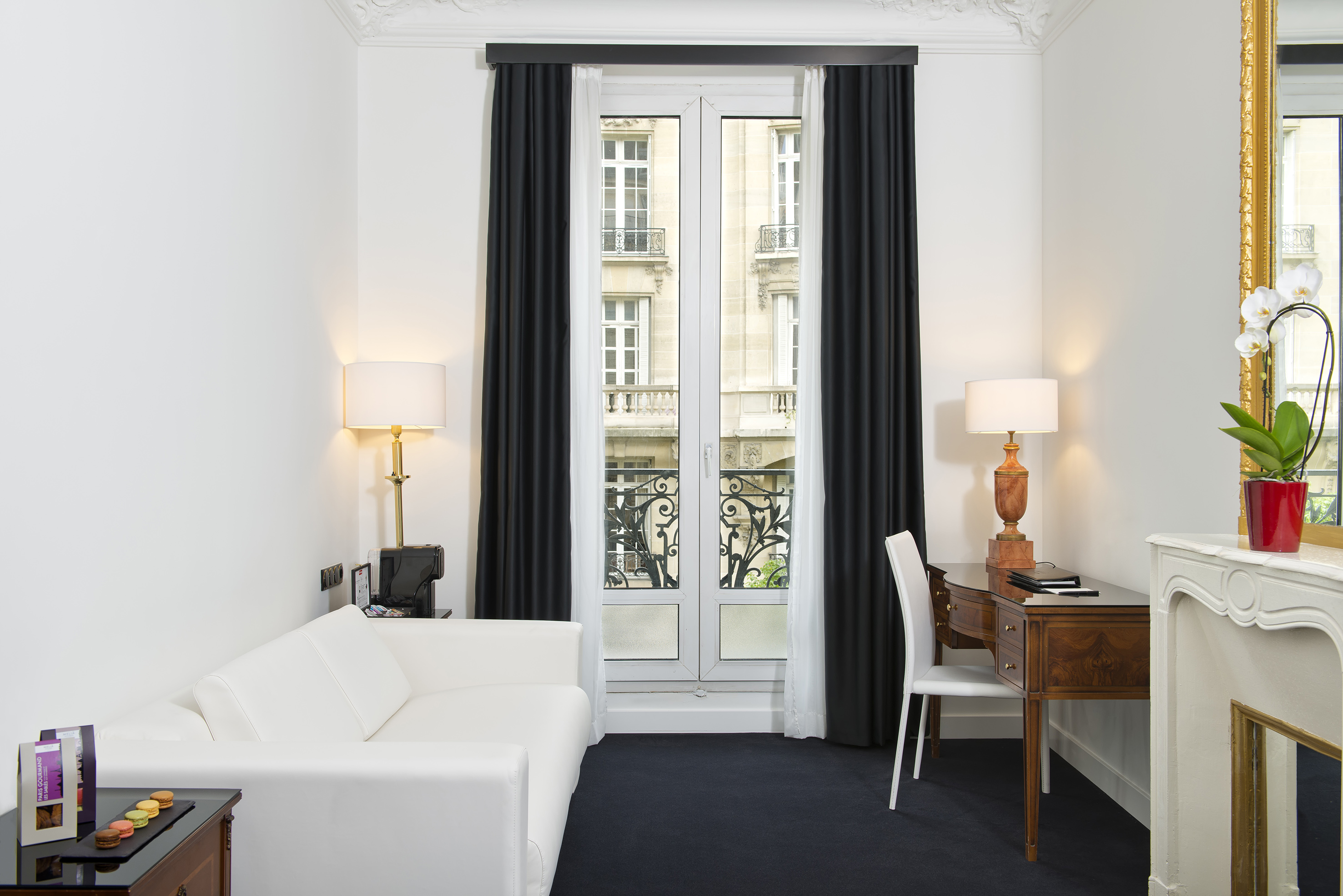 Elegant Parisian hotel room with white sofa, dark desk, and city view window.