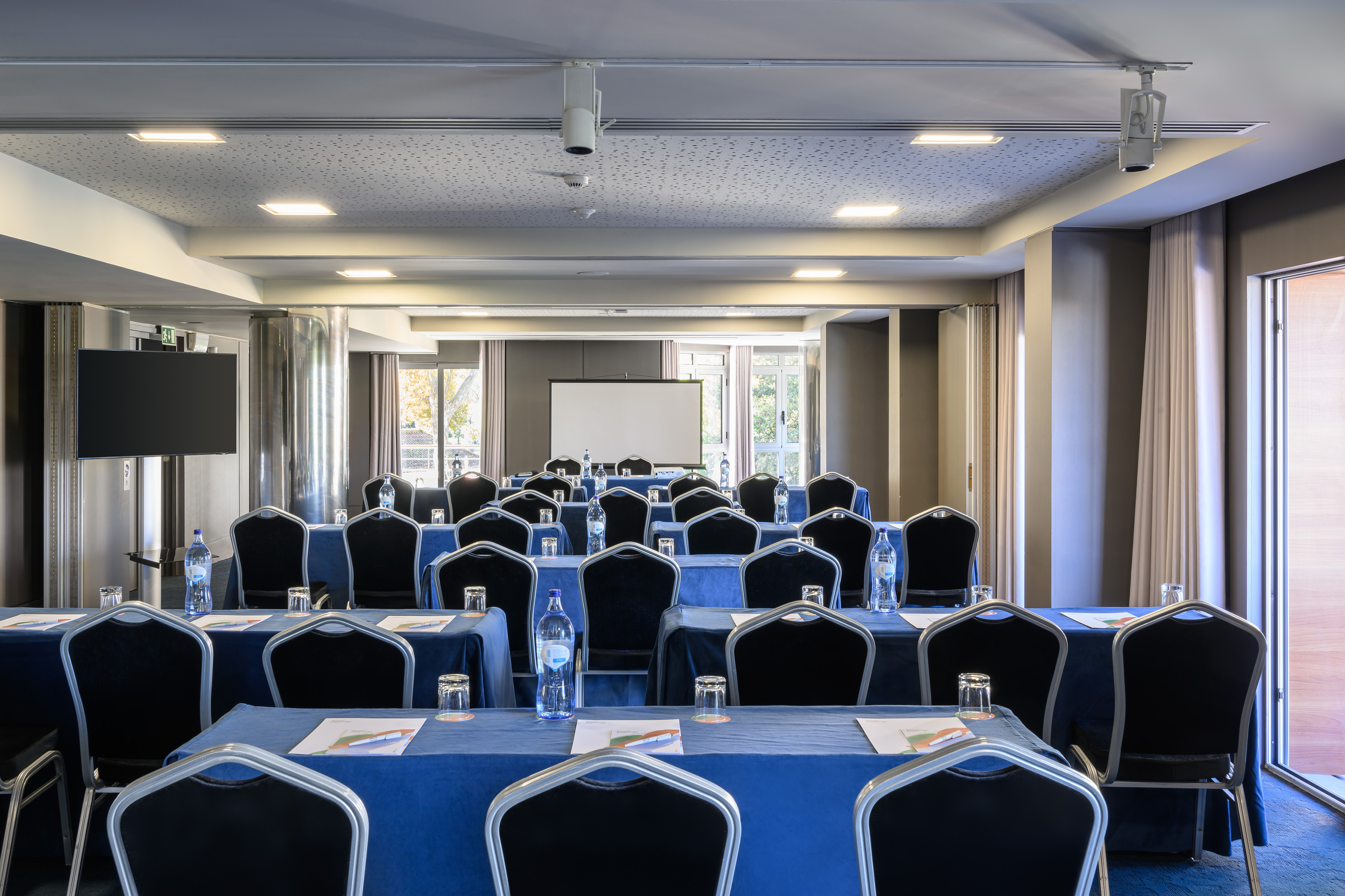 Conference room with blue tables, chairs, projection screen, and windows.