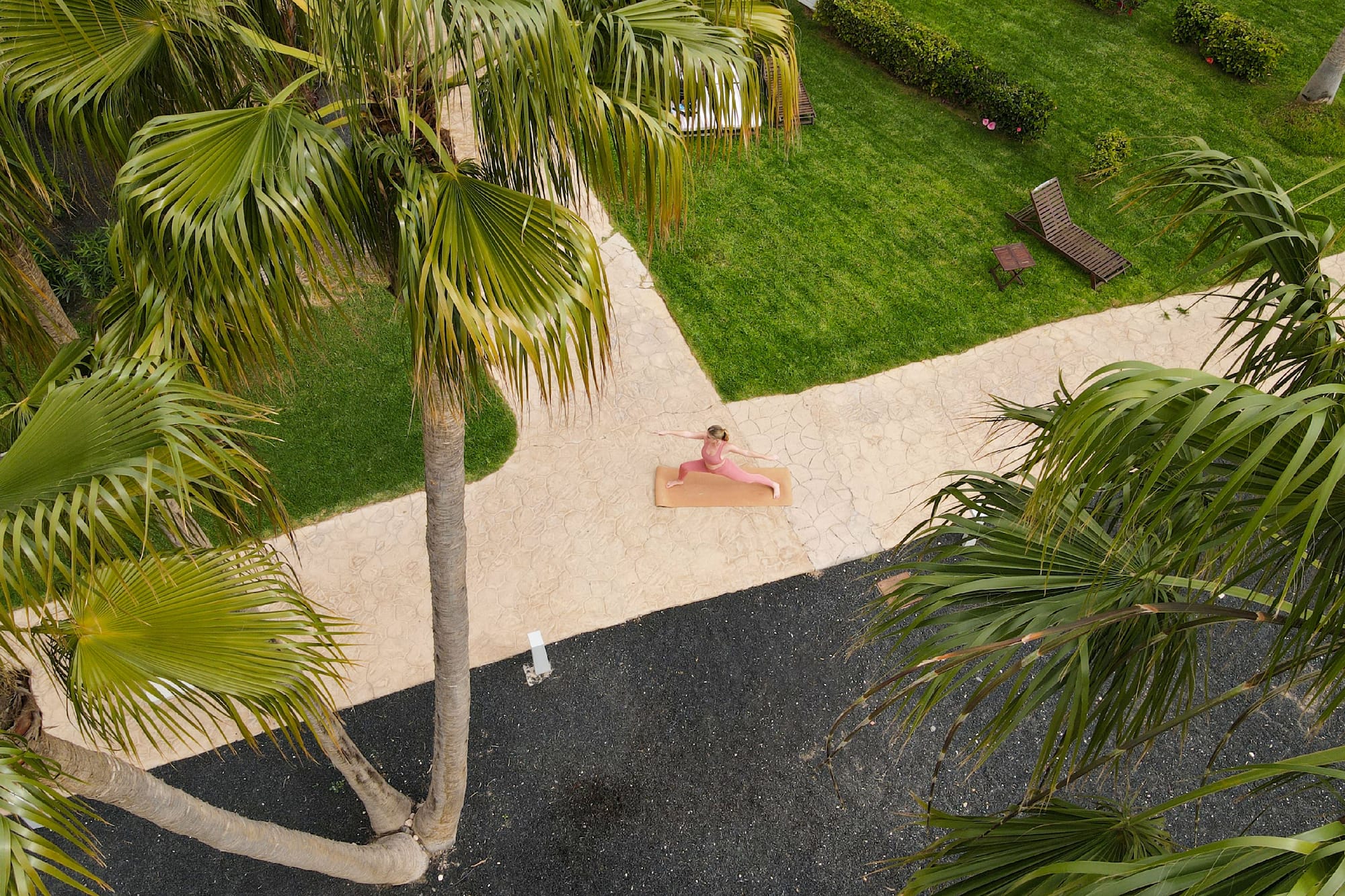 Woman in pink doing Warrior II yoga outdoors among palm trees.