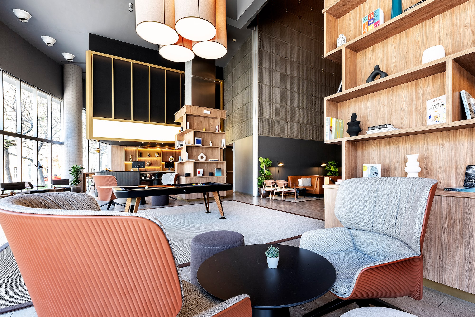 Contemporary lounge with orange armchairs, wooden shelves, and a billiards table.