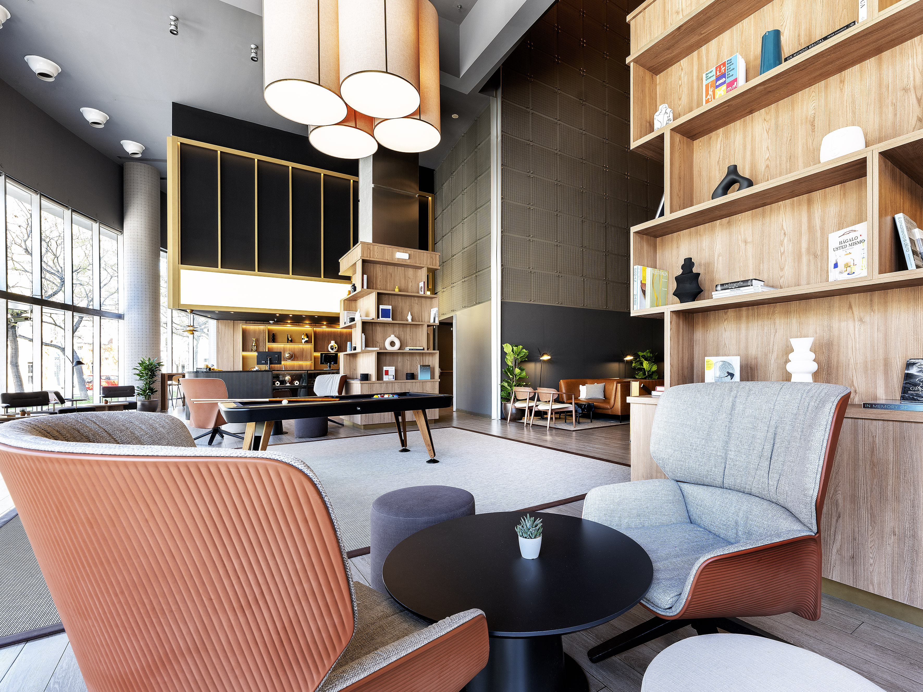 Contemporary lounge with orange armchairs, wooden shelves, and a billiards table.
