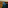 Aerial sunset over reservoir, forested mountains, distant city, and ocean.