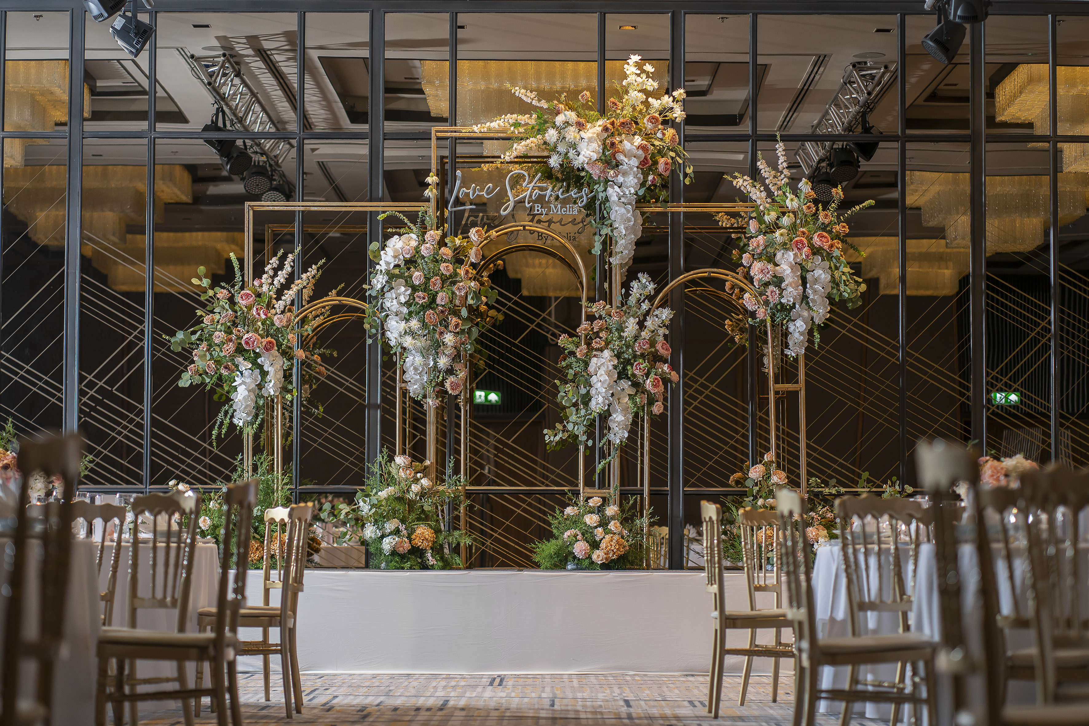 Wedding floral backdrop with gold geometric frames, flowers, 'Love Stories By Melià'.