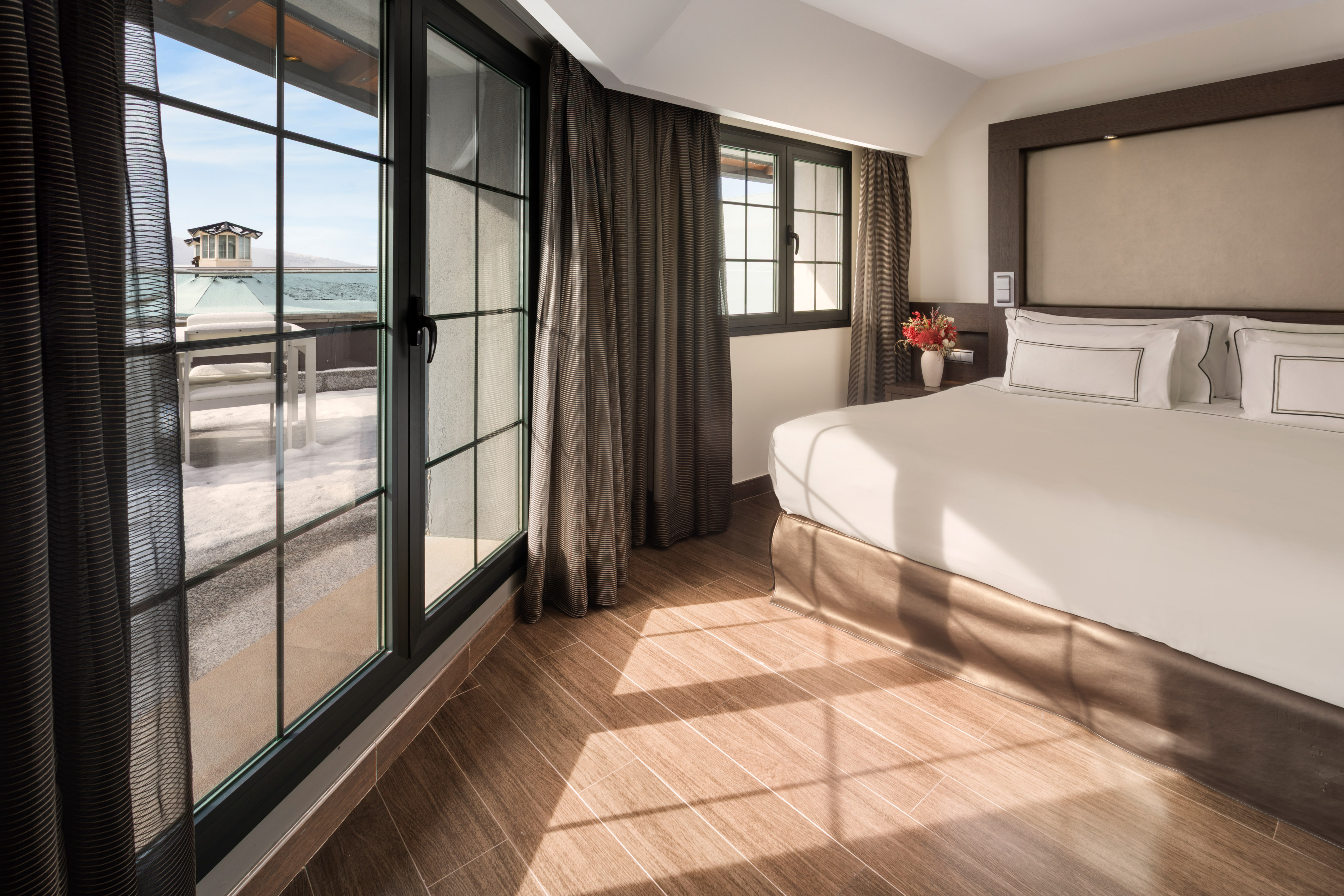 Modern bedroom with balcony view of snowy landscape. White bed, wooden floor.