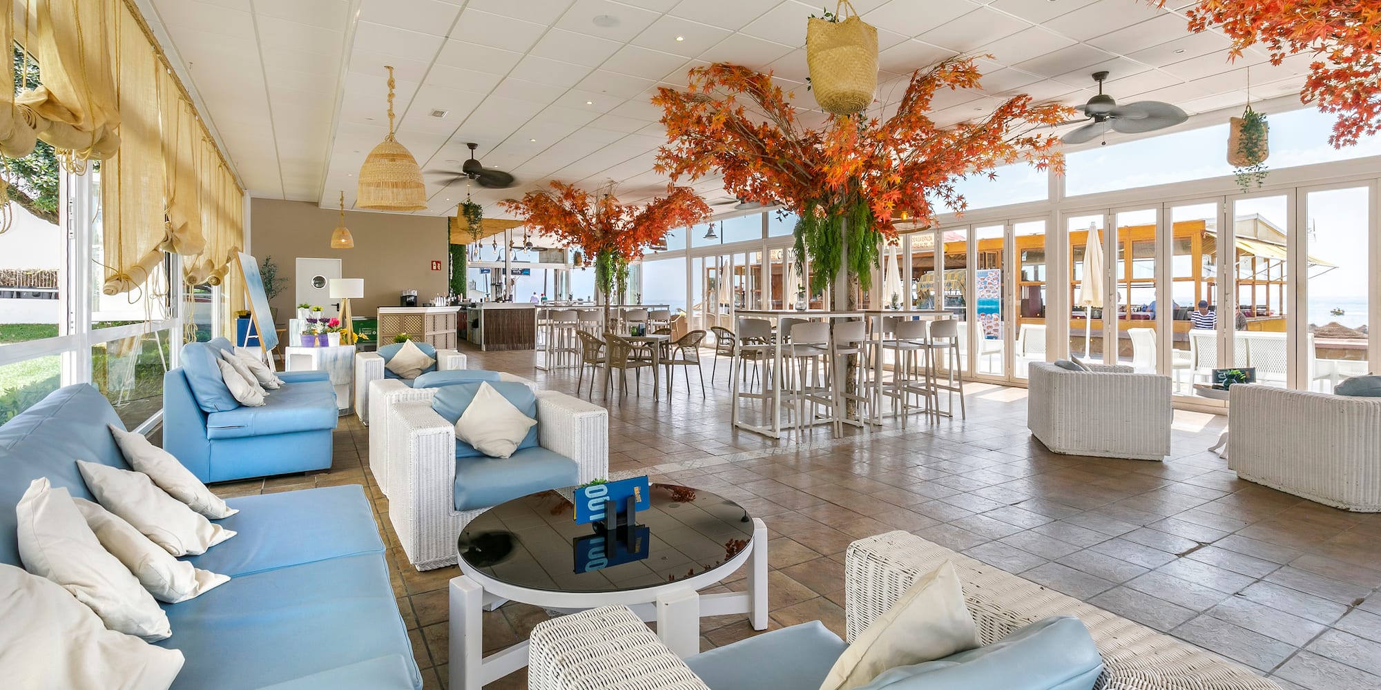 Modern lounge bar with blue seating, orange trees, and sea views.