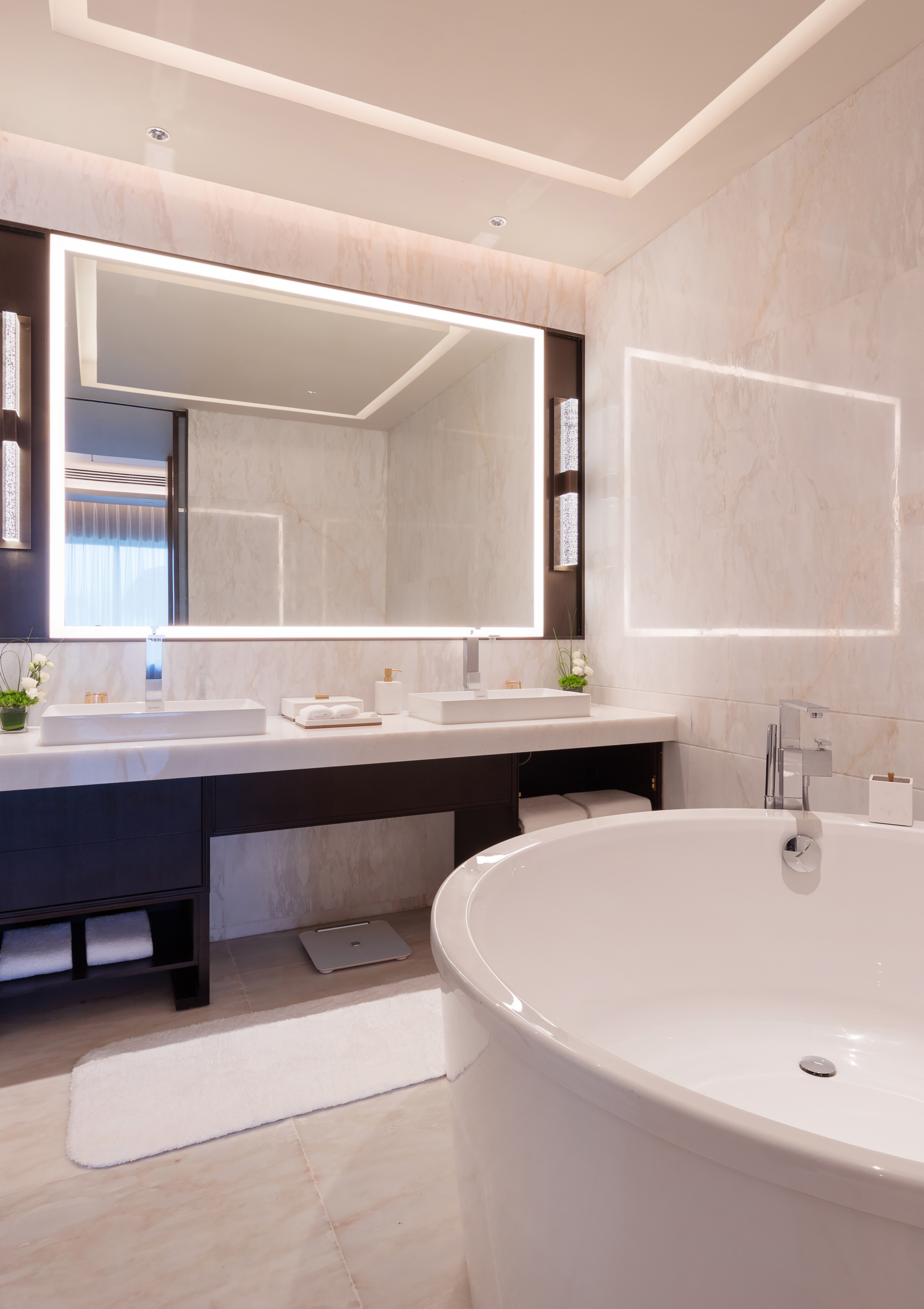 Spa-like luxury bathroom with freestanding tub and illuminated double vanity.