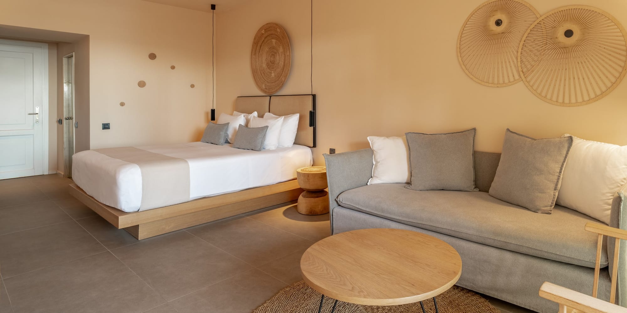 Neutral hotel suite with bed, sofa, coffee table, and contemporary decor.