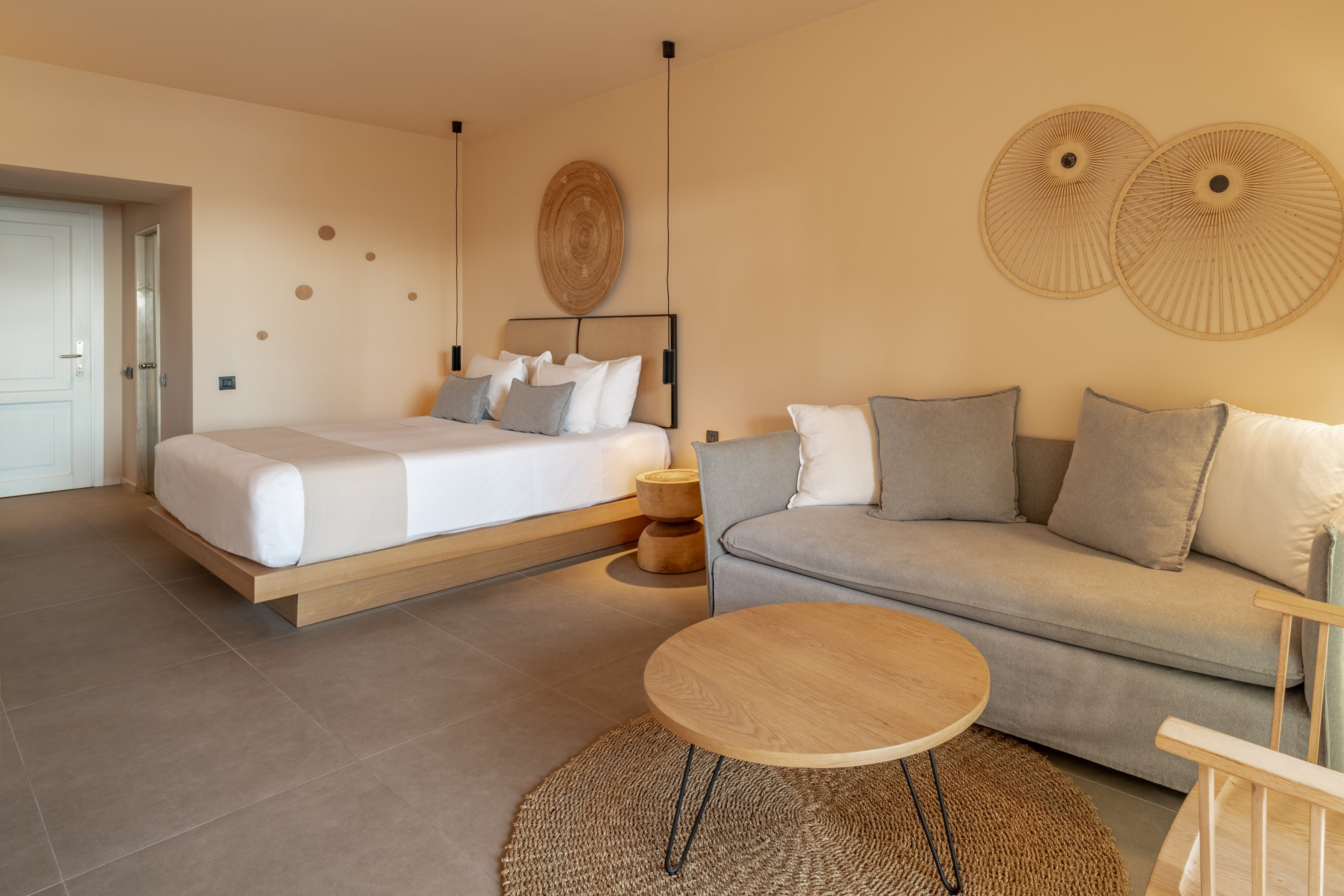 Neutral hotel suite with bed, sofa, coffee table, and contemporary decor.